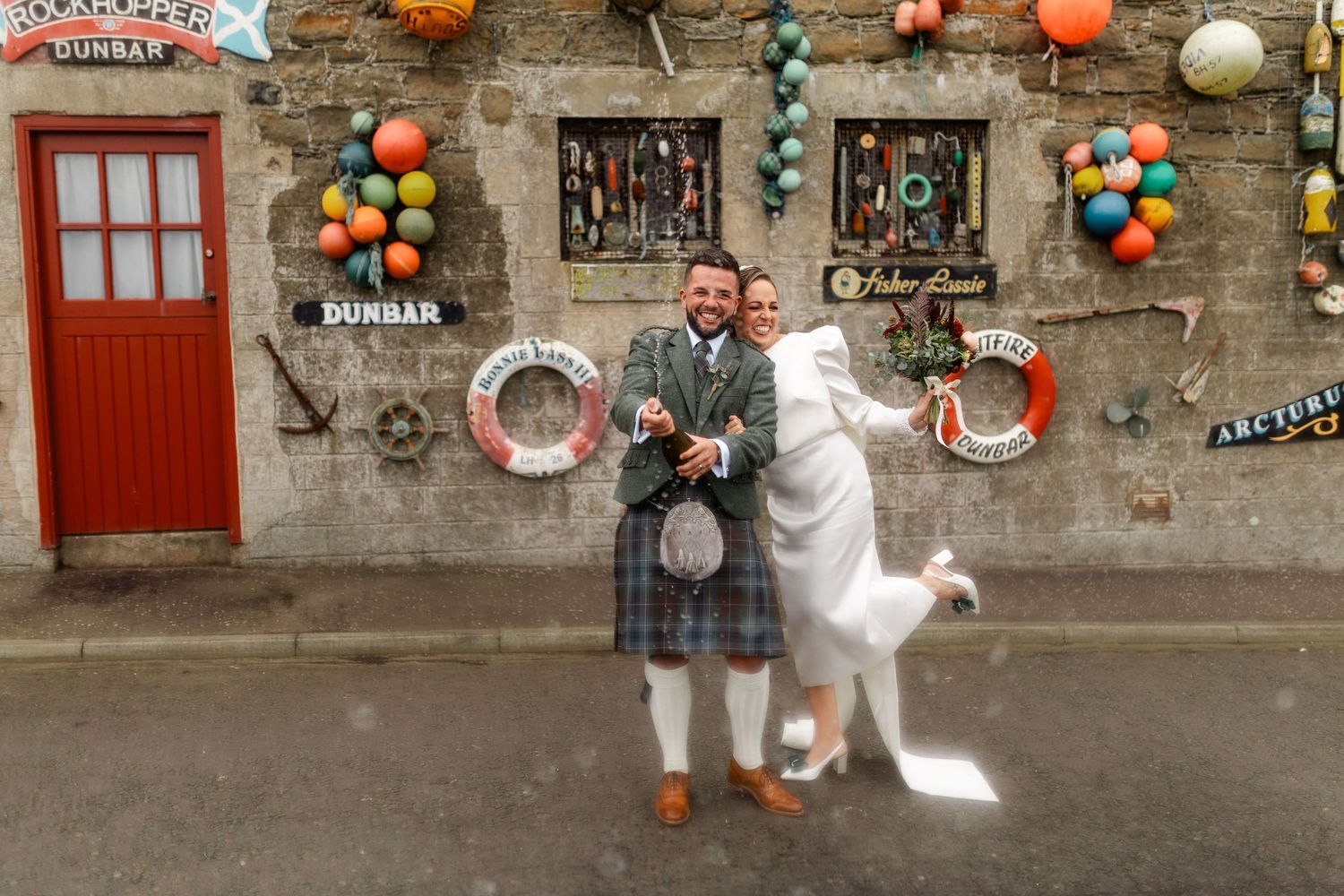 A stone wall decorated with colorful balloons, buoys, and various nautical items creating a festive seaside display.
