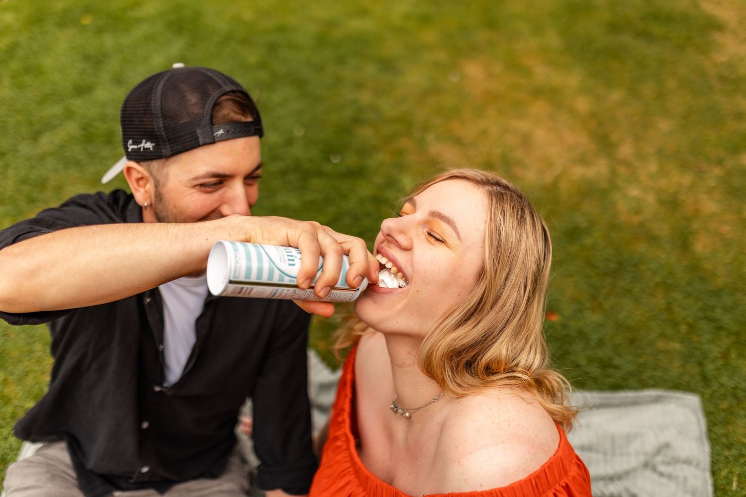 Playful couple feeding each other strawberries while relaxing outdoors.
