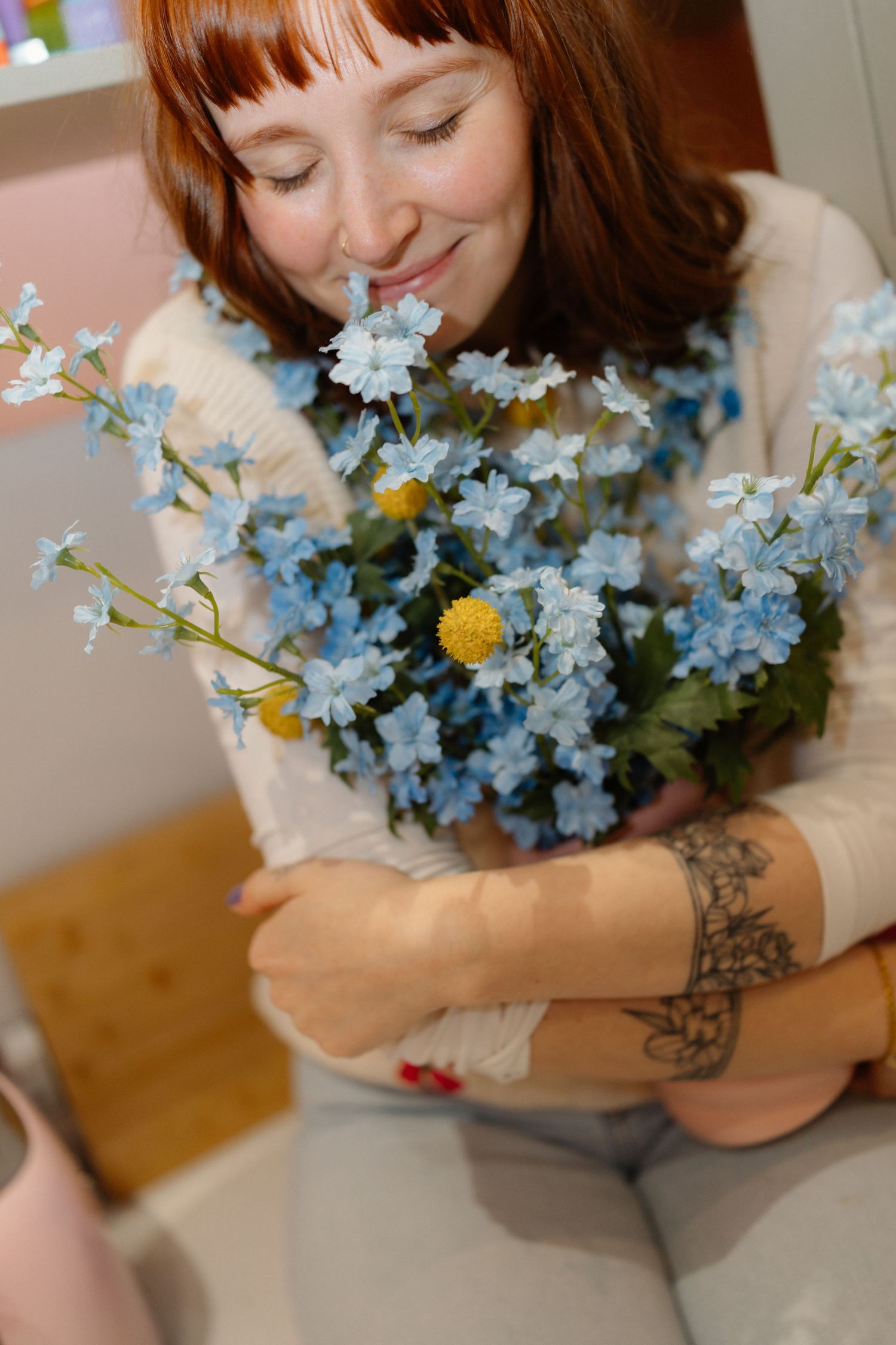 Holding a bouquet of light blue flowers with visible arm tattoo details.
