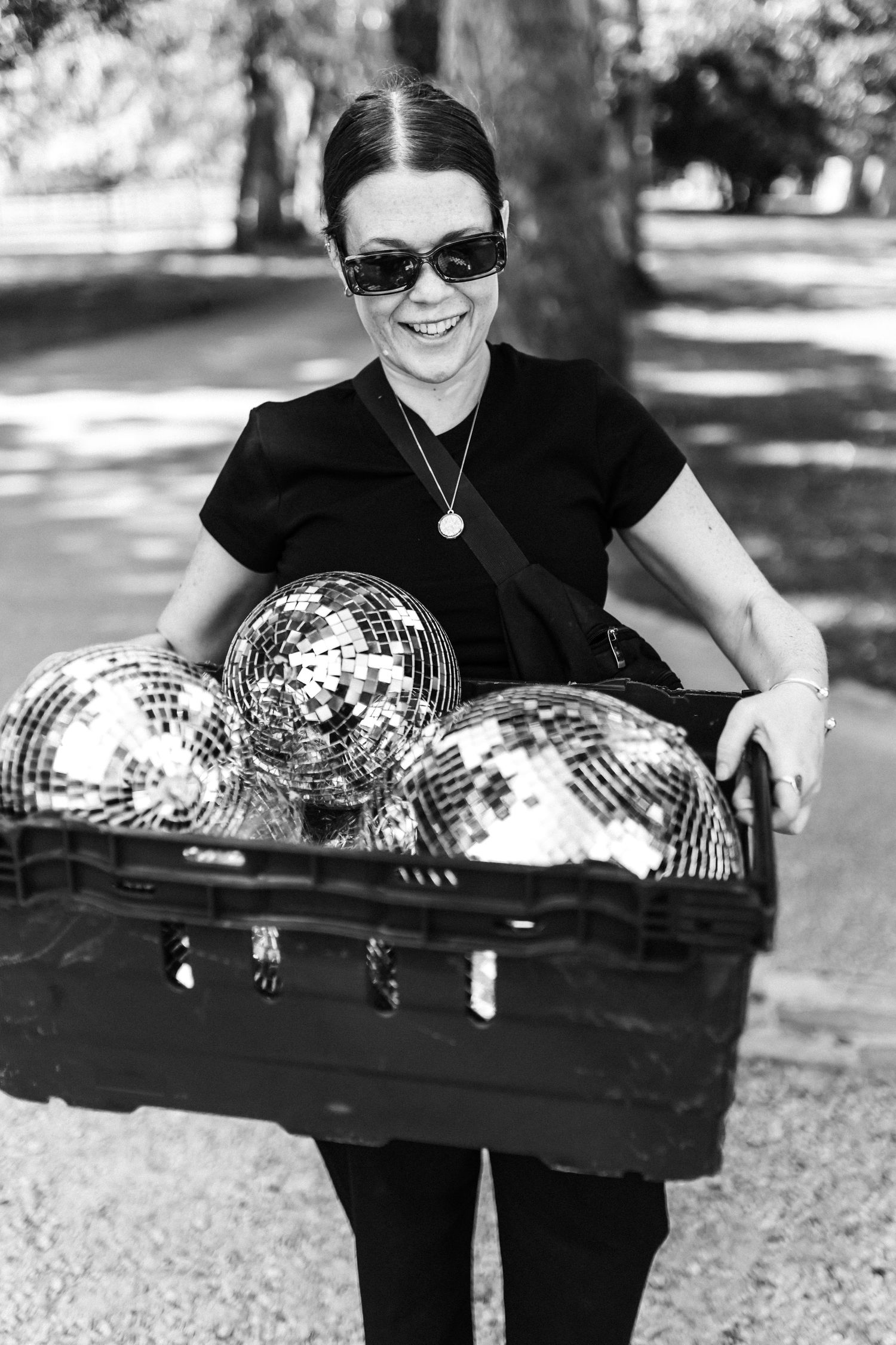 Person in black carrying a case of disco balls outdoors.