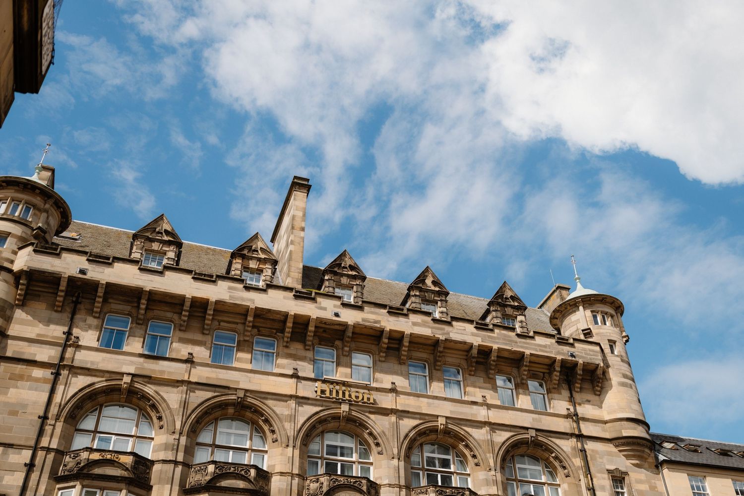 Historic stone building with ornate Gothic architecture against a blue sky with wispy clouds.