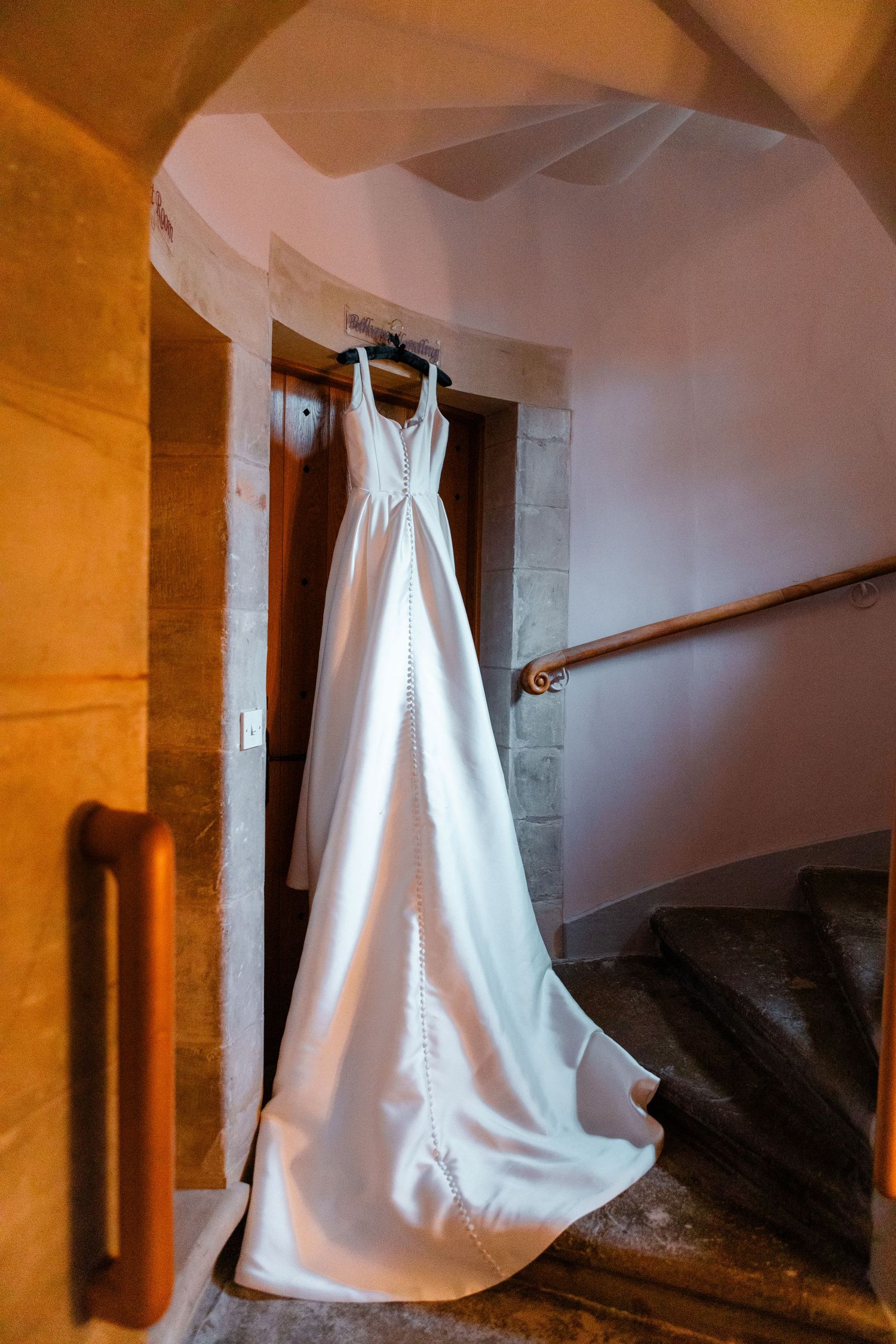 White wedding dress hangs gracefully against warm-toned castle walls.