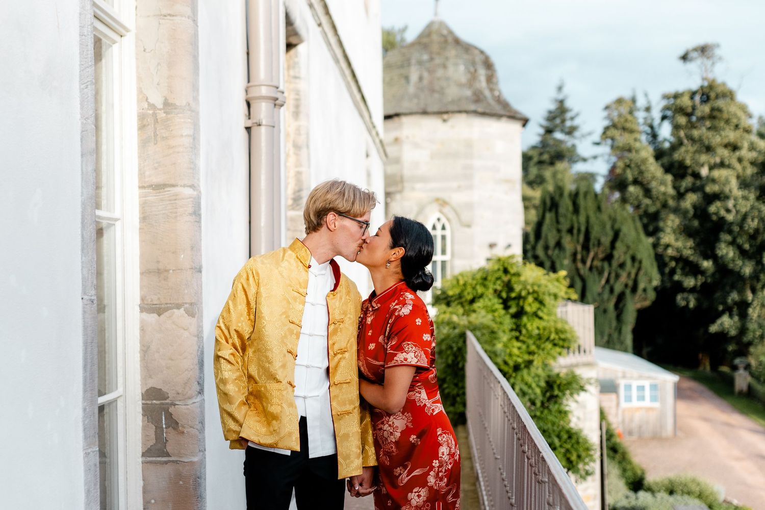 Couple sharing a romantic moment in front of a historic stone building with yellow and red outfits.