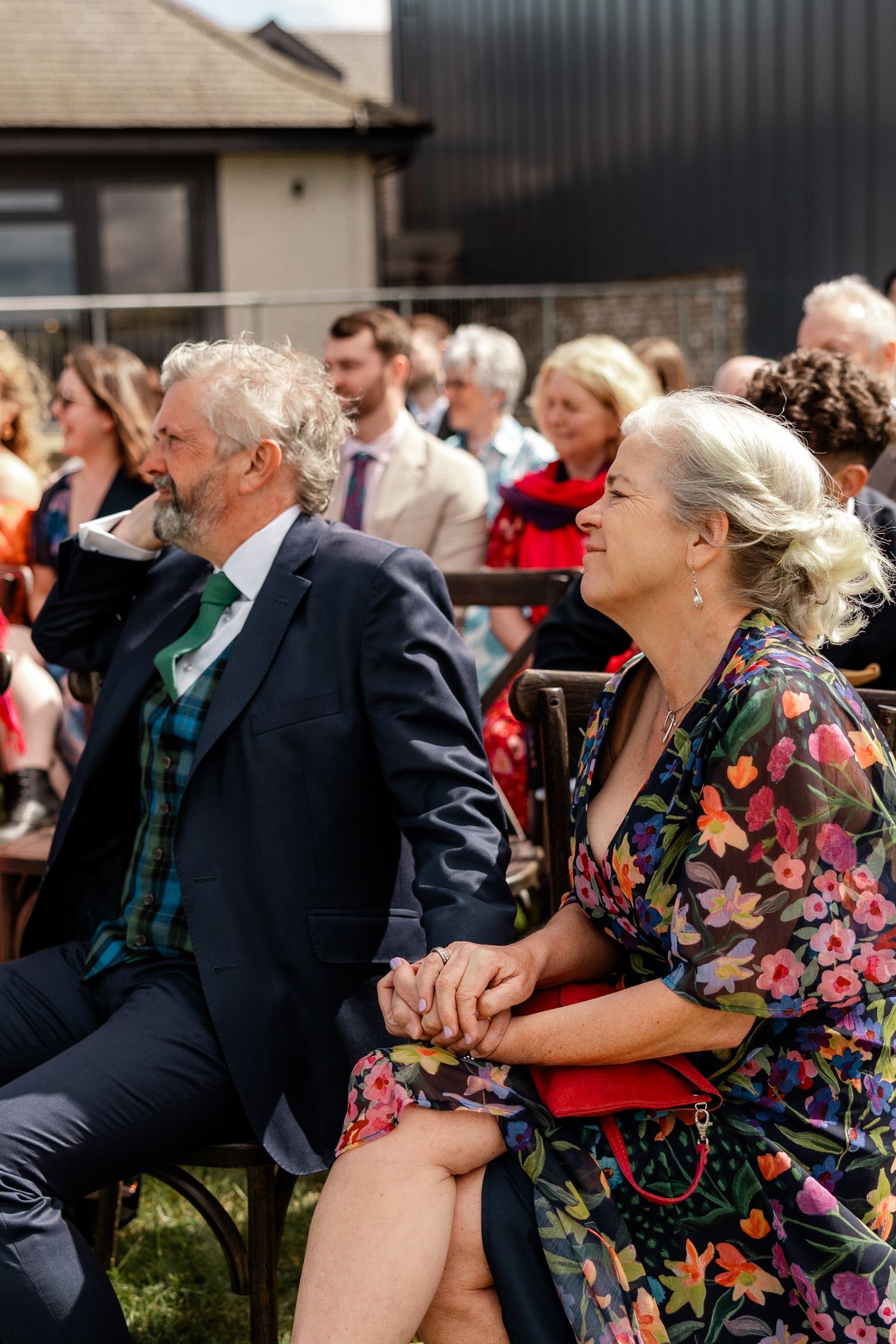 Guests in formal attire react emotionally during an outdoor wedding ceremony.