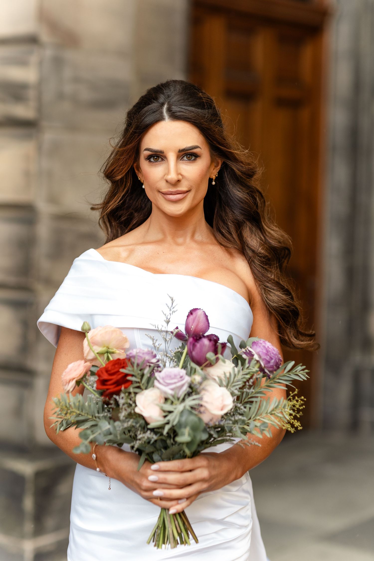 Elegant bridal portrait with a stunning bouquet featuring purple and red flowers.