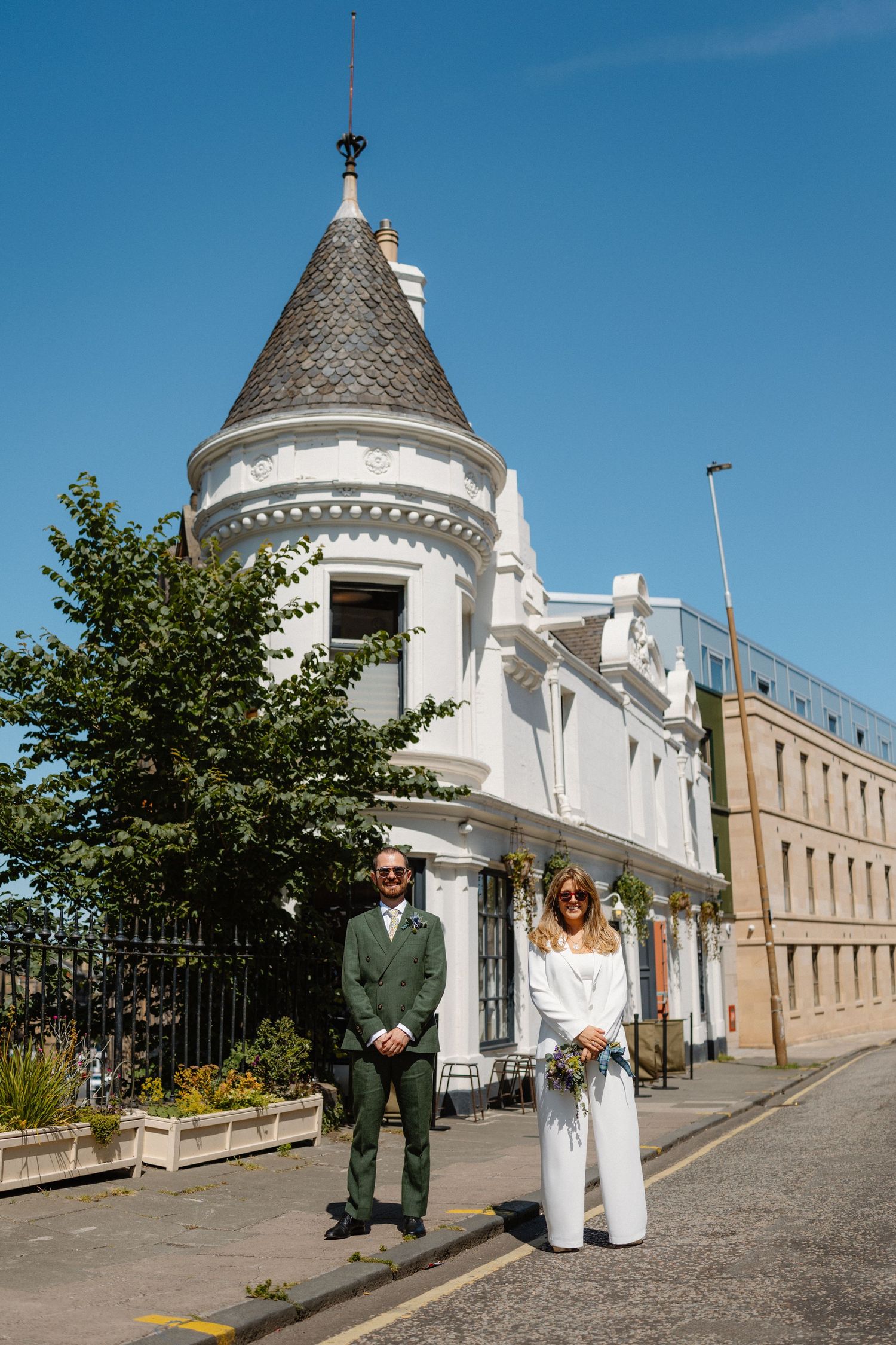 A couple posing outside a white castle-like building with turrets on a sunny day.