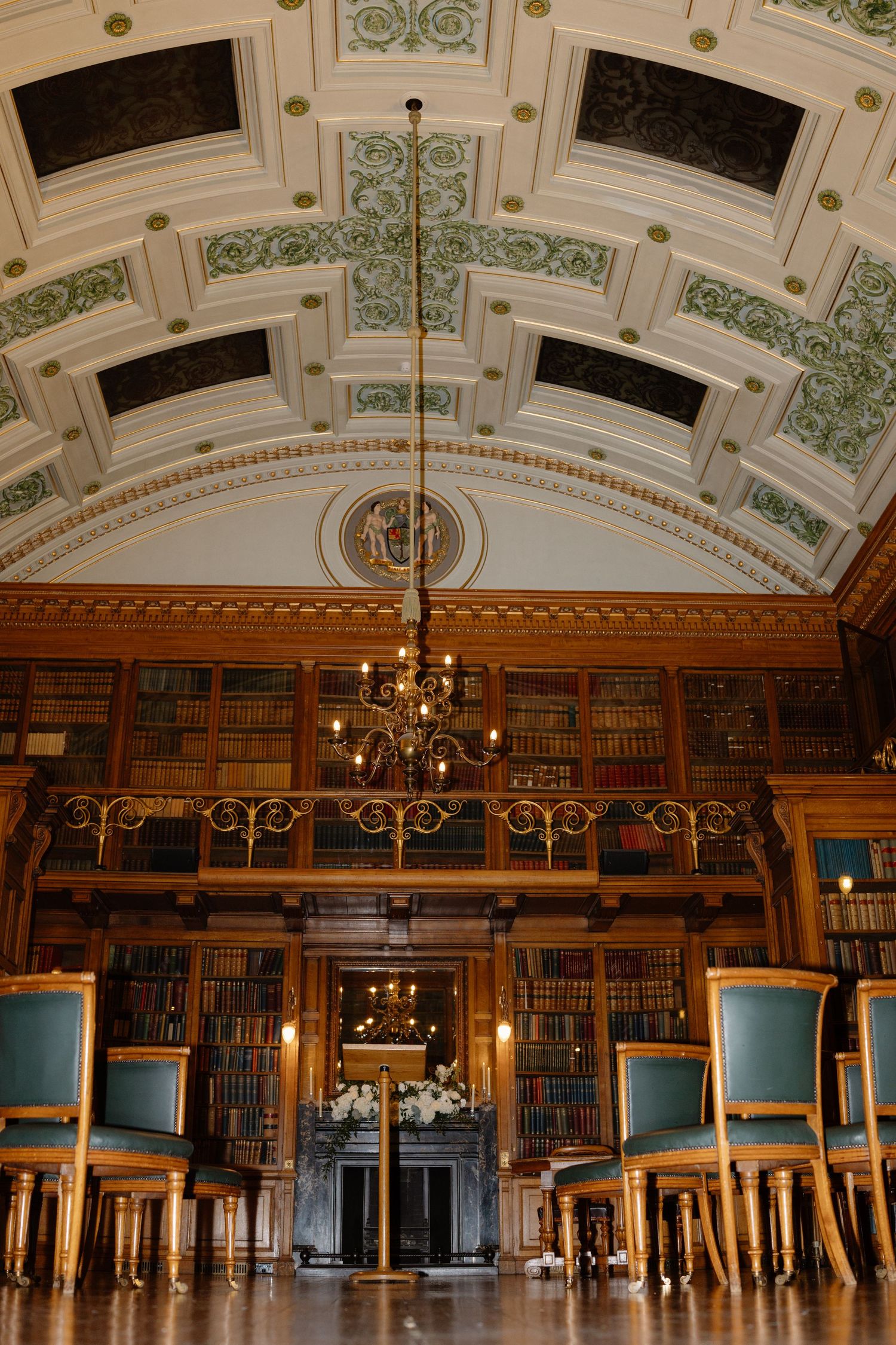 Panoramic view of an ornate historic library interior with turquoise chairs and elegant chandeliers beneath a decorative ceiling.