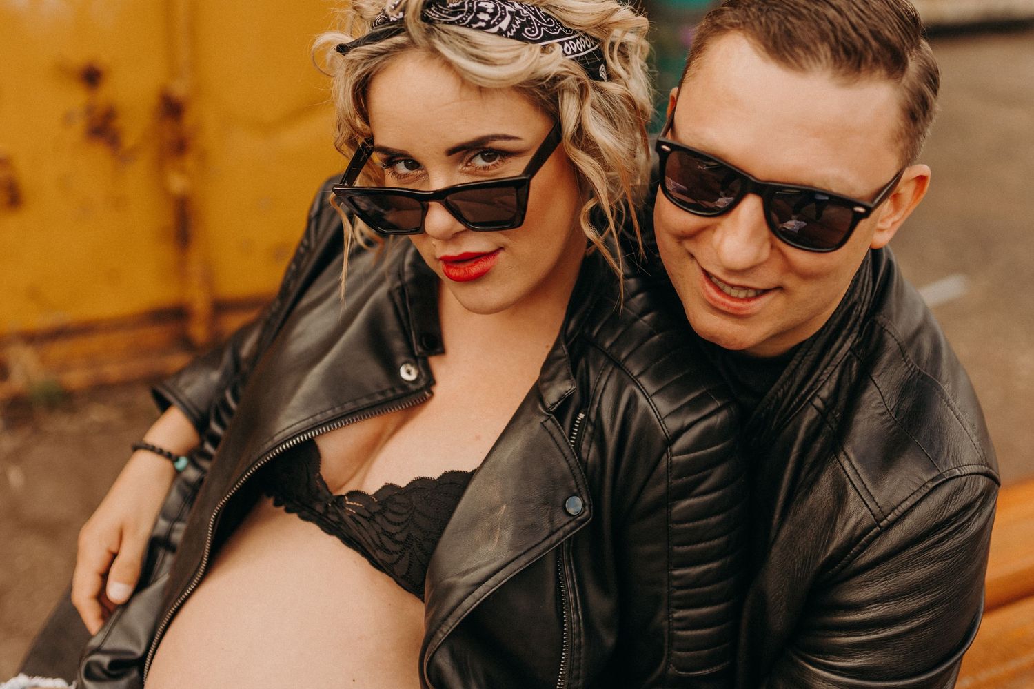 Couple in leather jackets posing against orange industrial background.