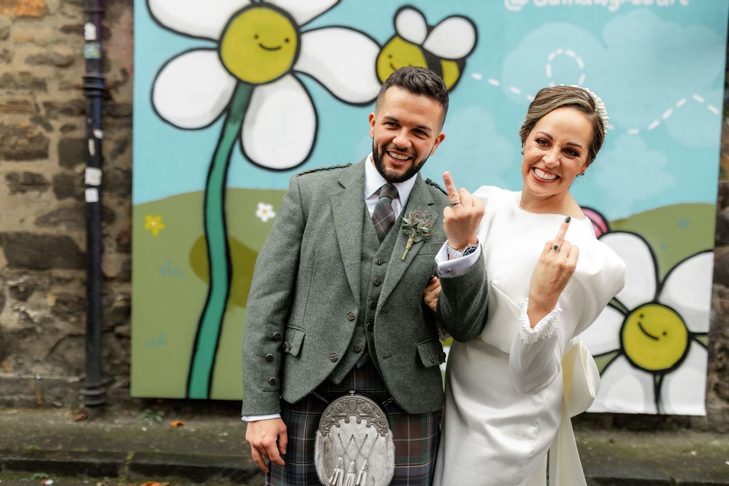 Wedding couple poses in front of a whimsical mural featuring cartoon daisies on a blue background.