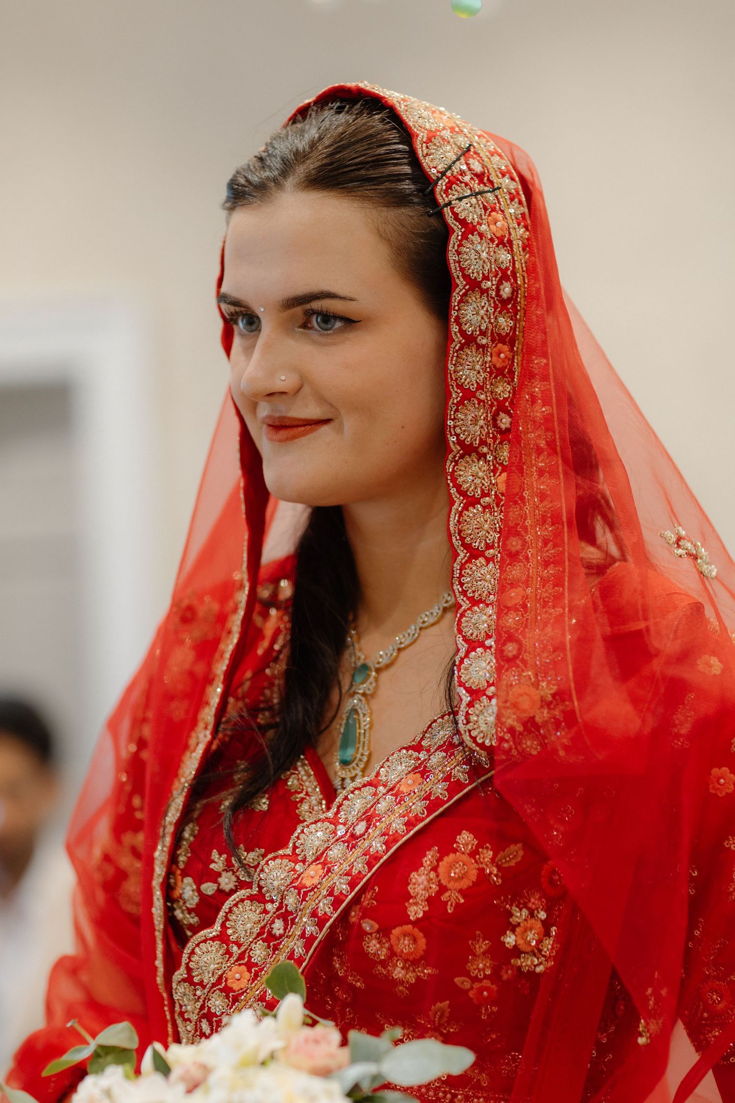 Beautiful bride wearing traditional red Indian bridal lehenga with embroidered dupatta veil holding a bouquet.