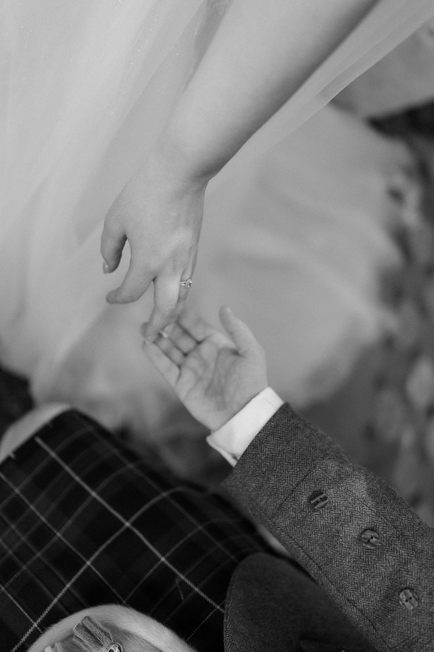Black and white photo of bride and groom holding hands, groom wearing tartan kilt at Scottish wedding.