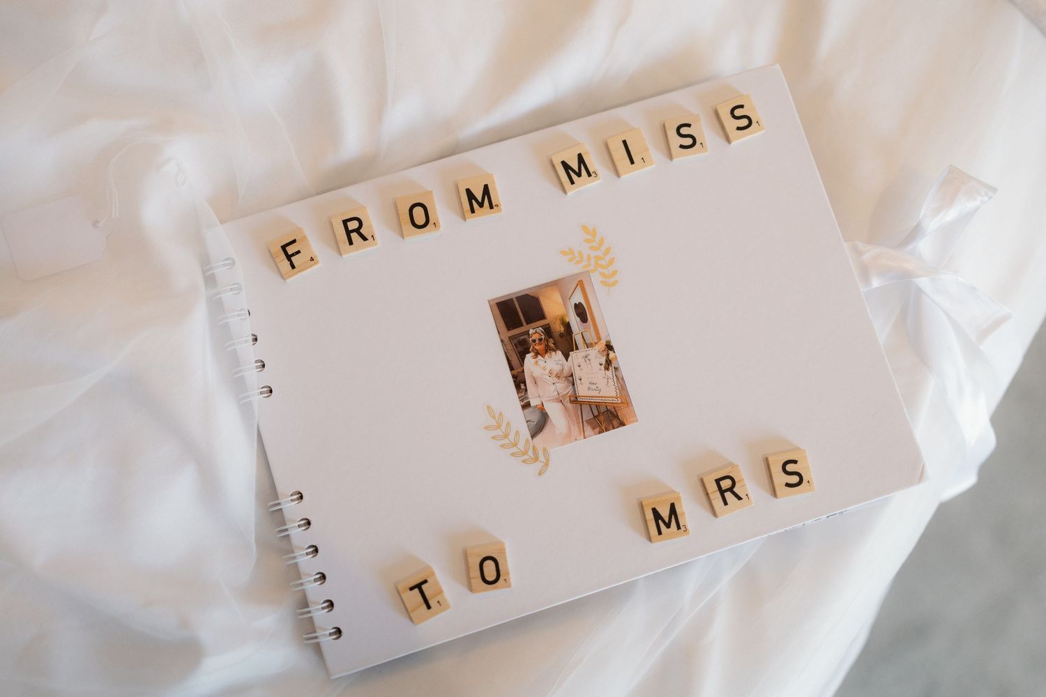 Wedding guest book decorated with scrabble tiles spelling From Miss To Mrs with couple photo.