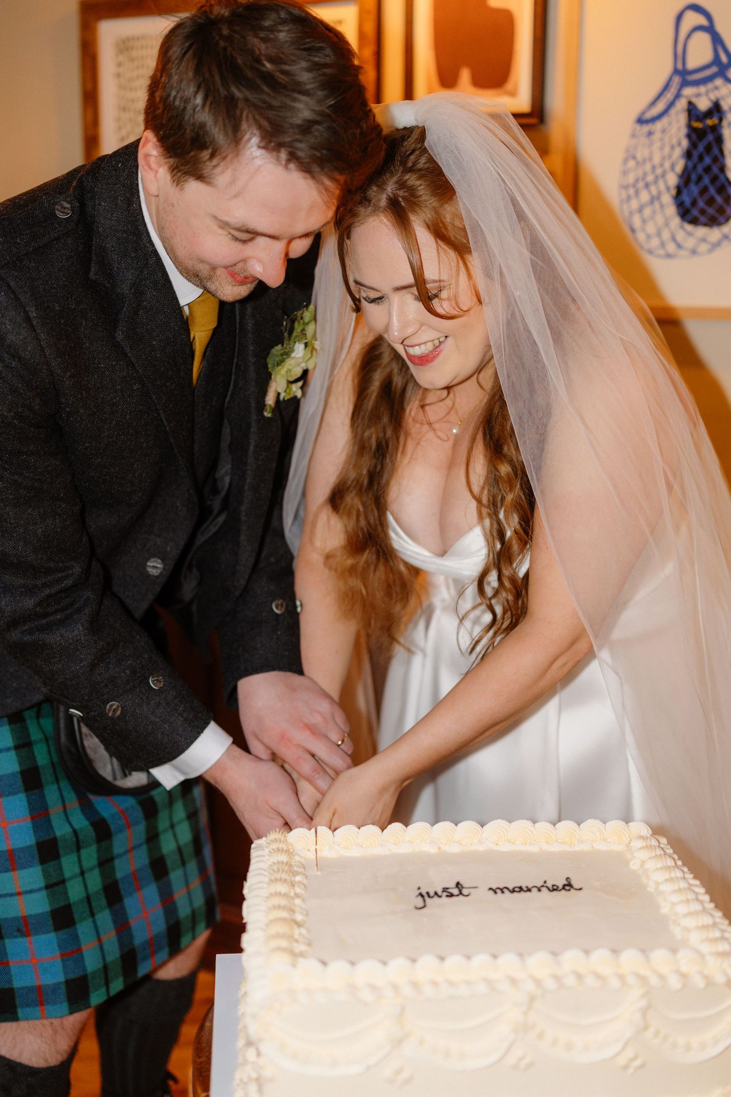 Newlyweds cutting white wedding cake inscribed with just married at reception.