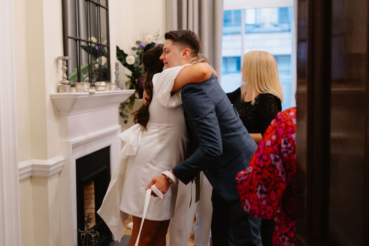 Bride and groom share a warm hug near a fireplace during their intimate wedding ceremony.