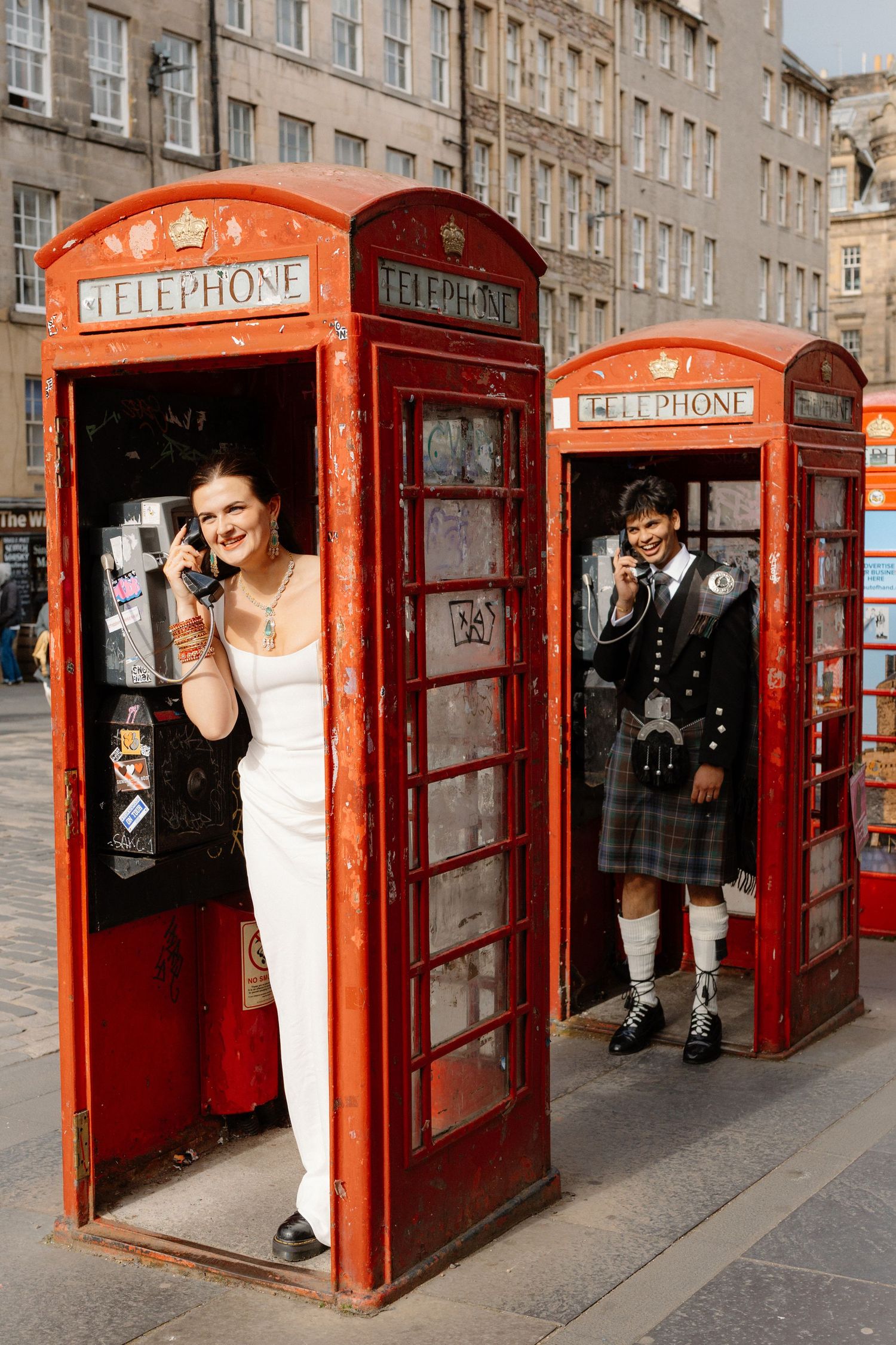Bride and groom posing in iconic red British telephone boxes on Edinburgh's Royal Mile.