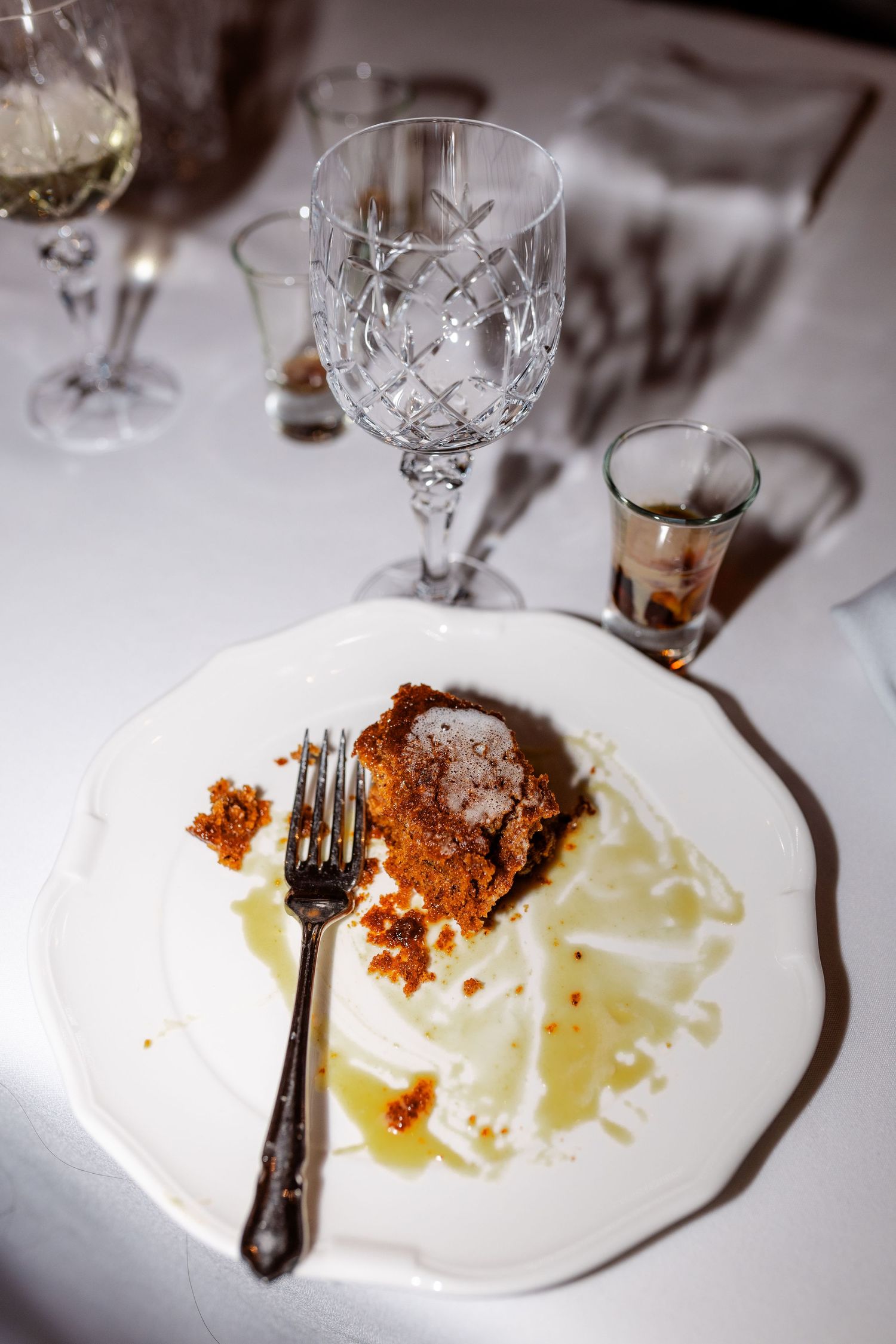 Partially eaten elegant dessert with crumble topping on white plate beside crystal glassware at wedding reception dinner.
