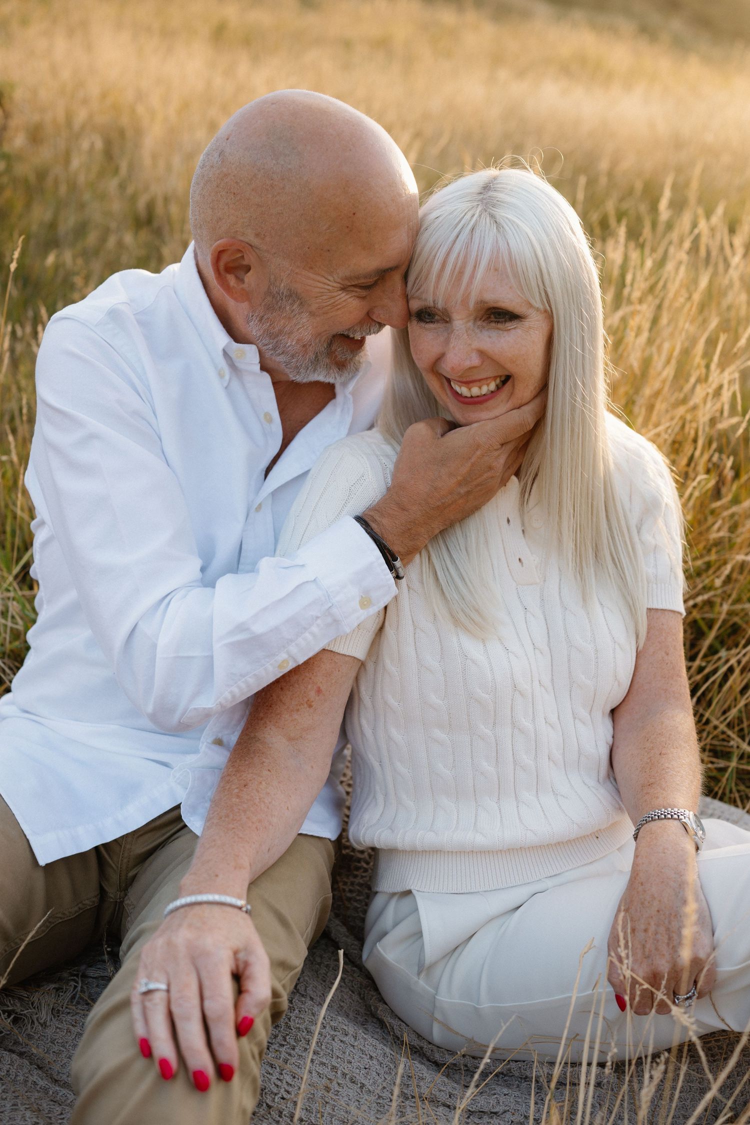 Candid moment of a couple laughing together in a golden wheat field at sunset.