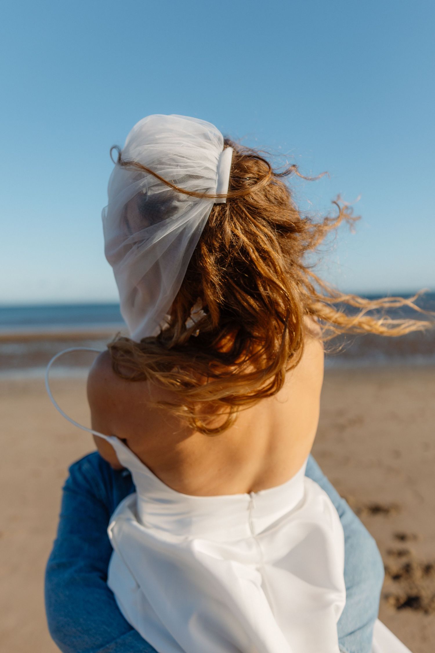 Wind-swept hair and white fabric against a blue sky at the beach.