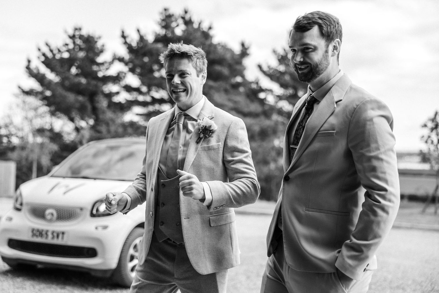 Groomsmen in grey suits chatting and laughing outdoors.