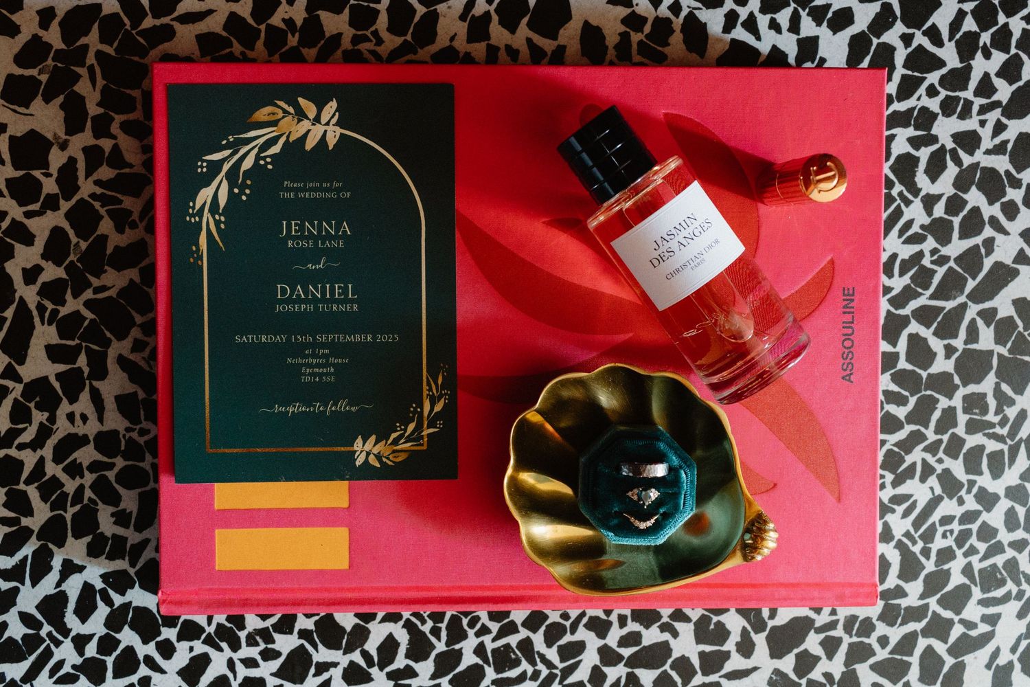 Elegant wedding invitation with gold botanical design beside a red perfume bottle on a pink tray.