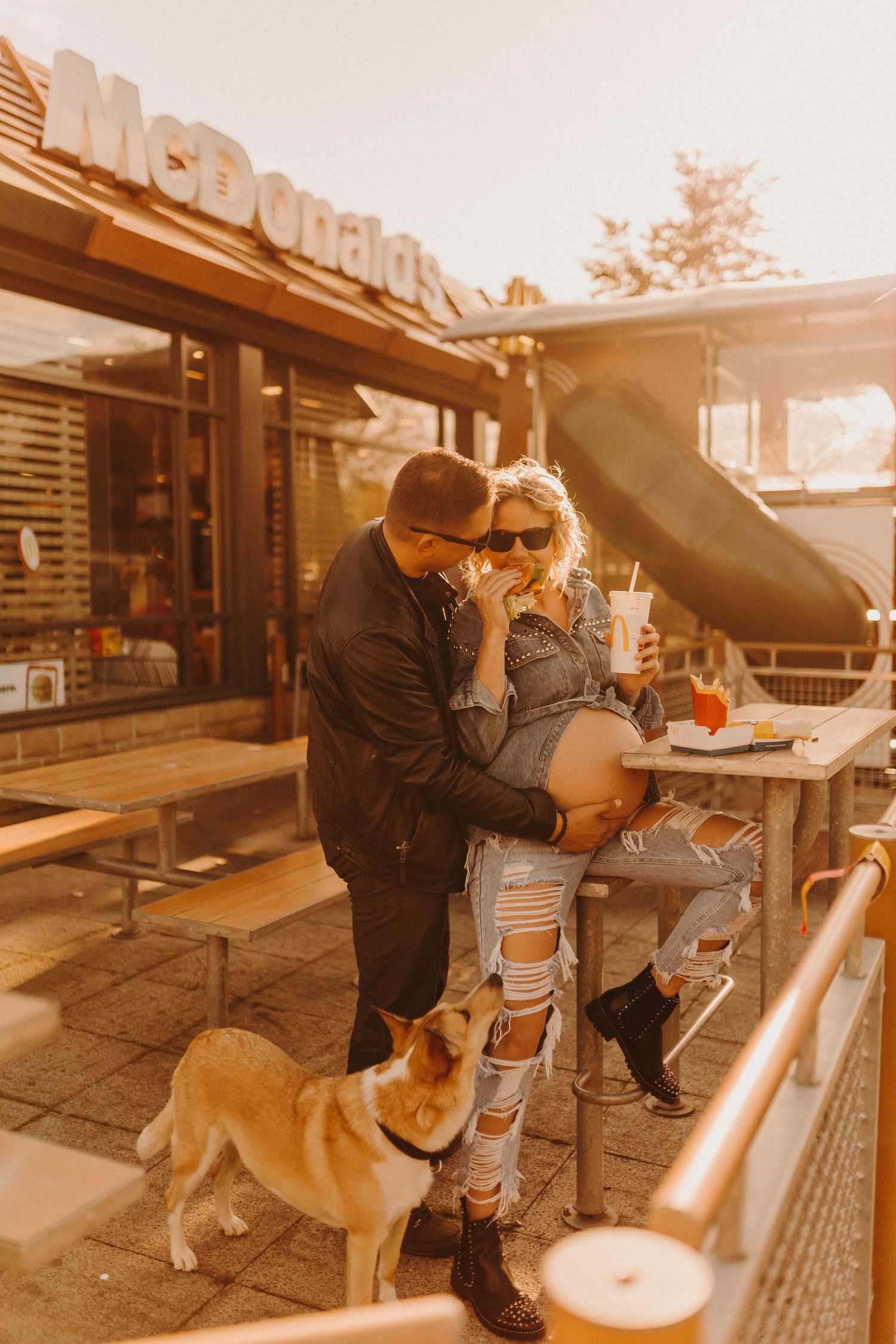 Couple sharing fast food with their dog outside a restaurant at sunset.