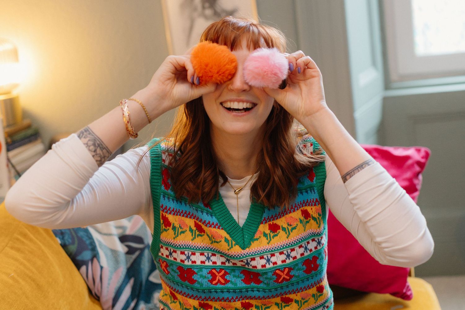 Person wearing colorful patterned sweater holding orange fruit playfully.