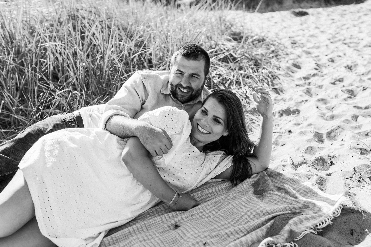 A family lounges together on a blanket in the grass during a casual outdoor photo session.