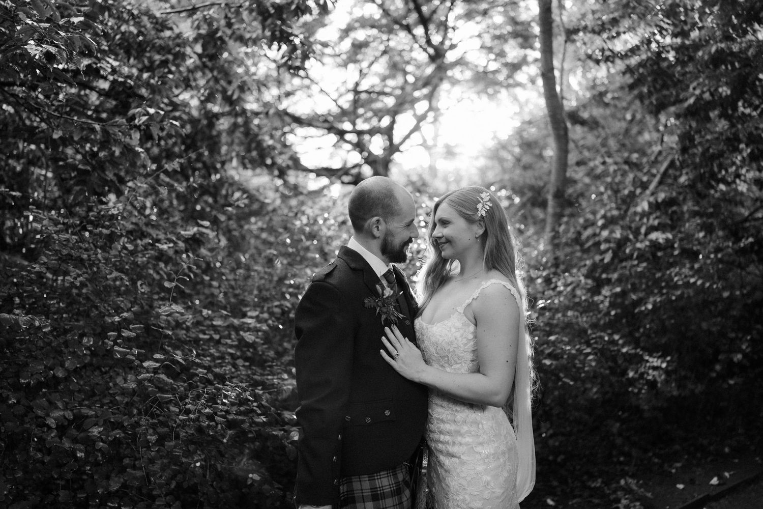 A romantic black and white photo of a couple dancing with umbrellas in a garden setting.