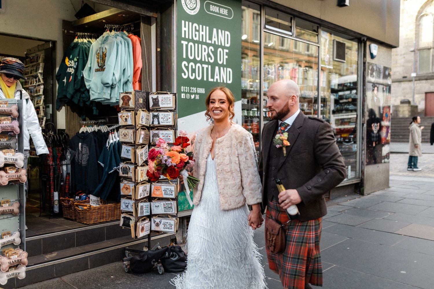 A couple poses outside a Tours of Scotland shop in traditional wedding attire.