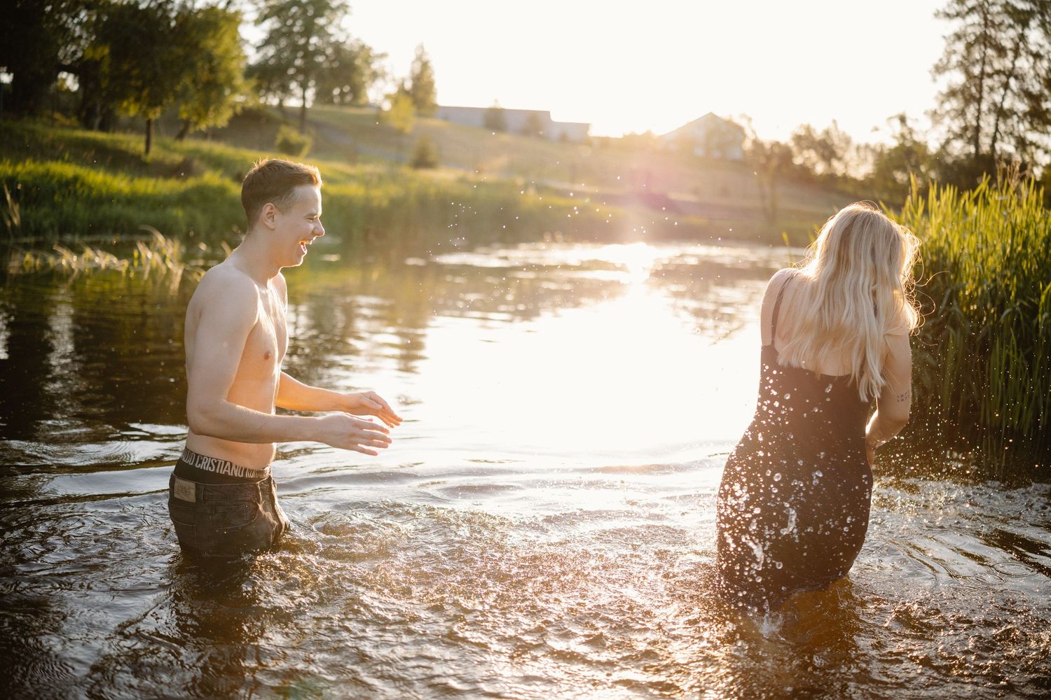 Couple splashing in lake water during golden hour sunset.