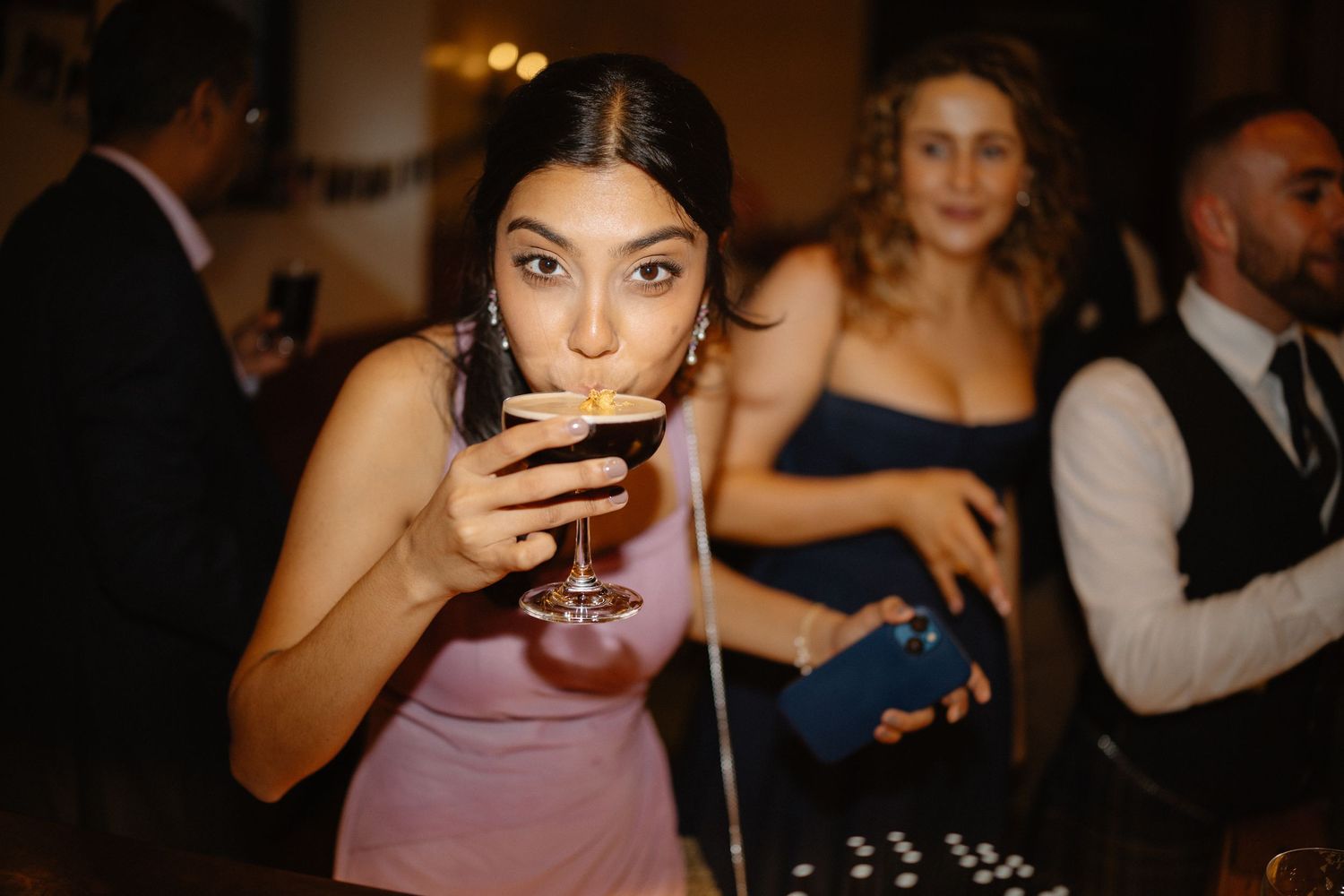Wedding guests enjoying drinks and dancing at a dimly lit reception party.