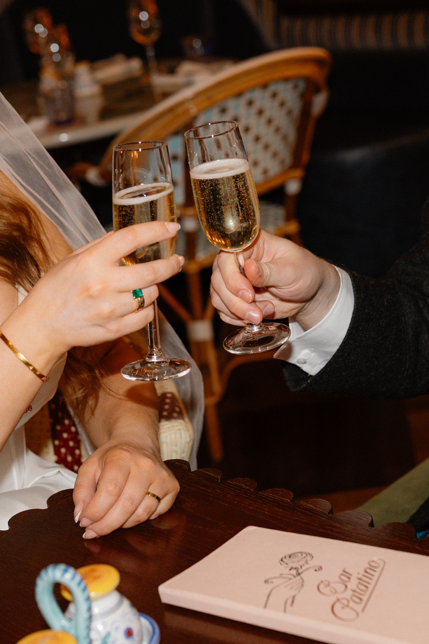 Bride and groom toasting with champagne flutes at wedding reception table, bride wearing emerald ring.