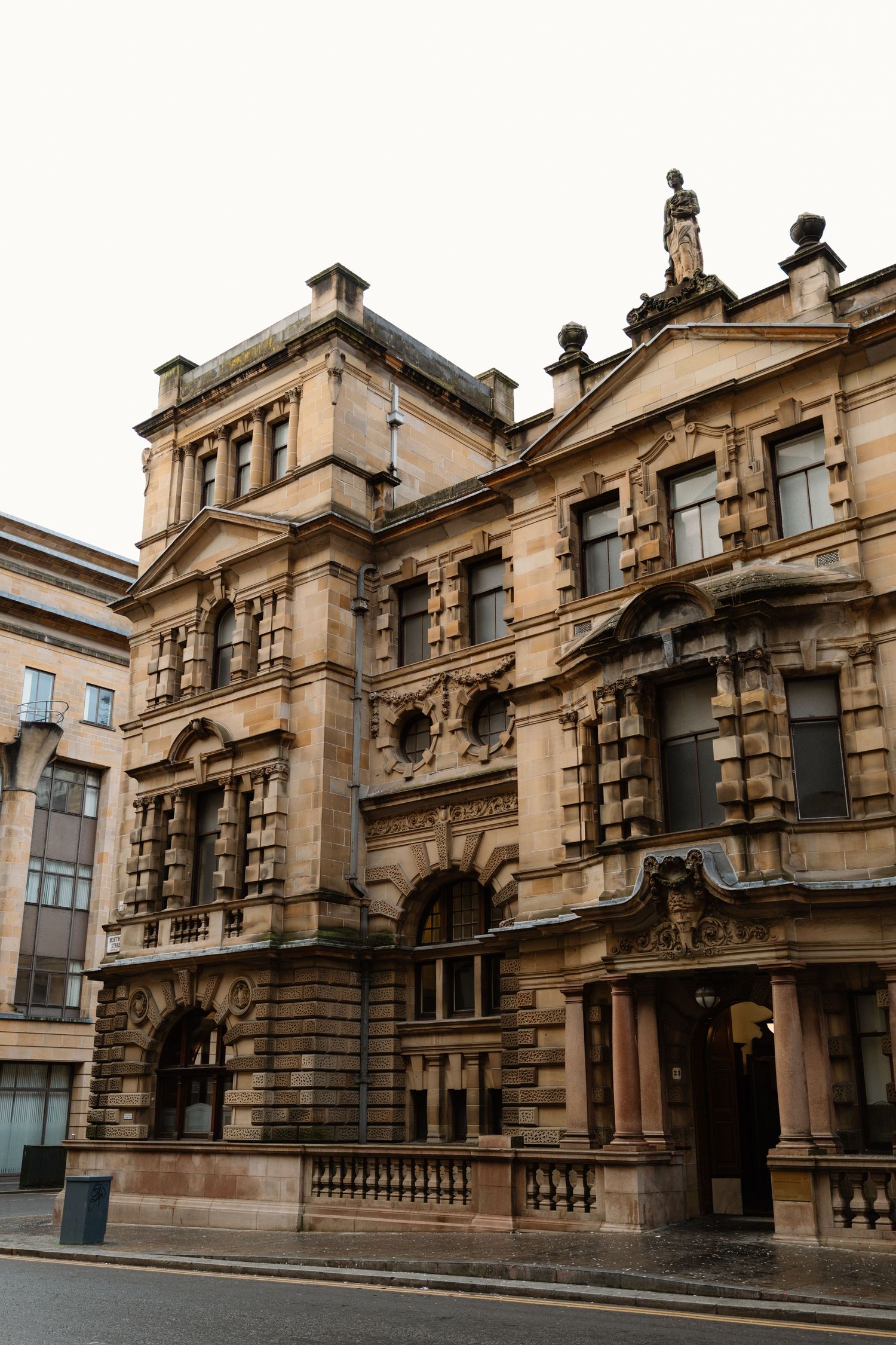 Grand Victorian sandstone building with ornate facade, arched windows, and classical sculptures on a quiet city street.