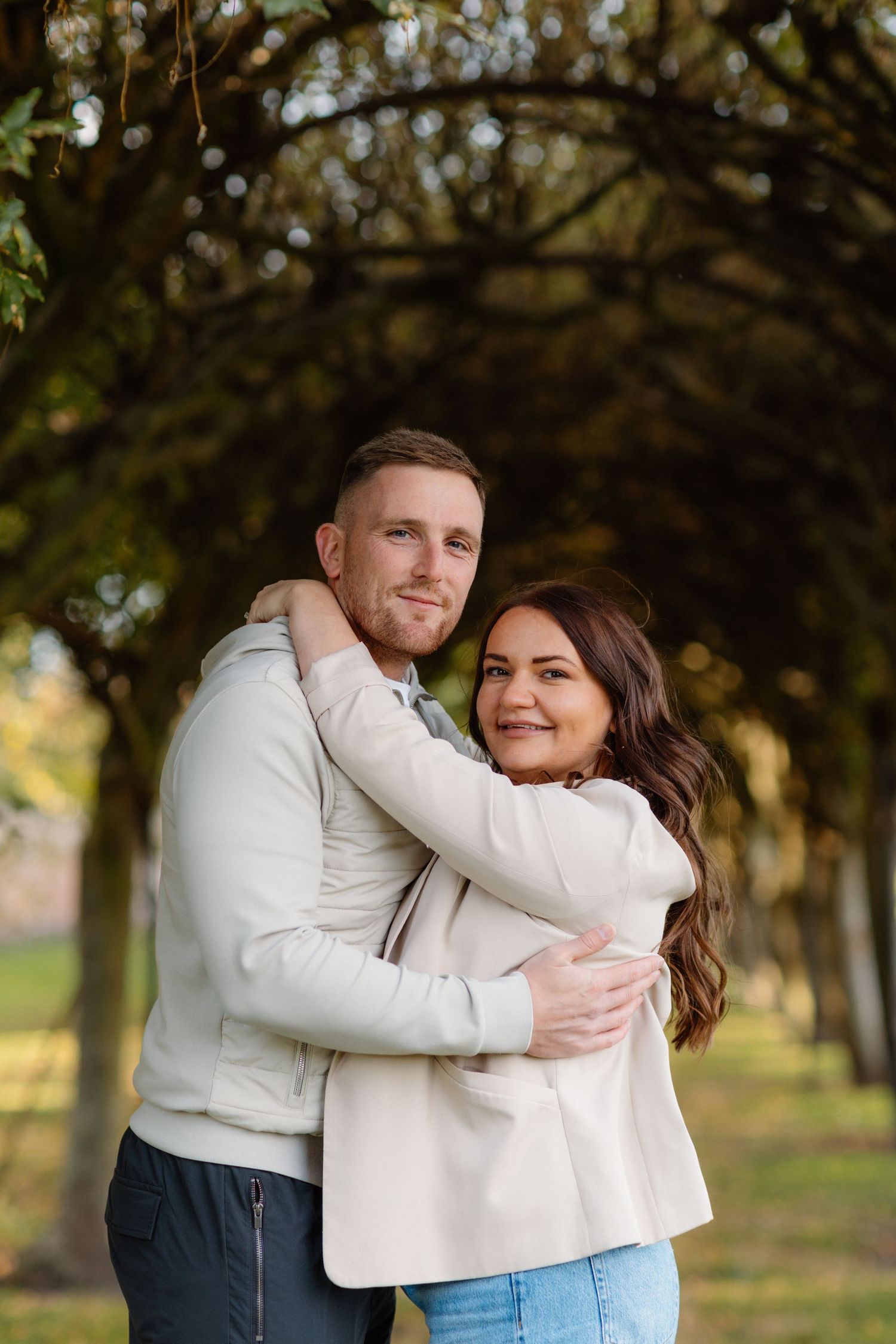 Couple embracing outdoors in casual white outfits during autumn photoshoot.