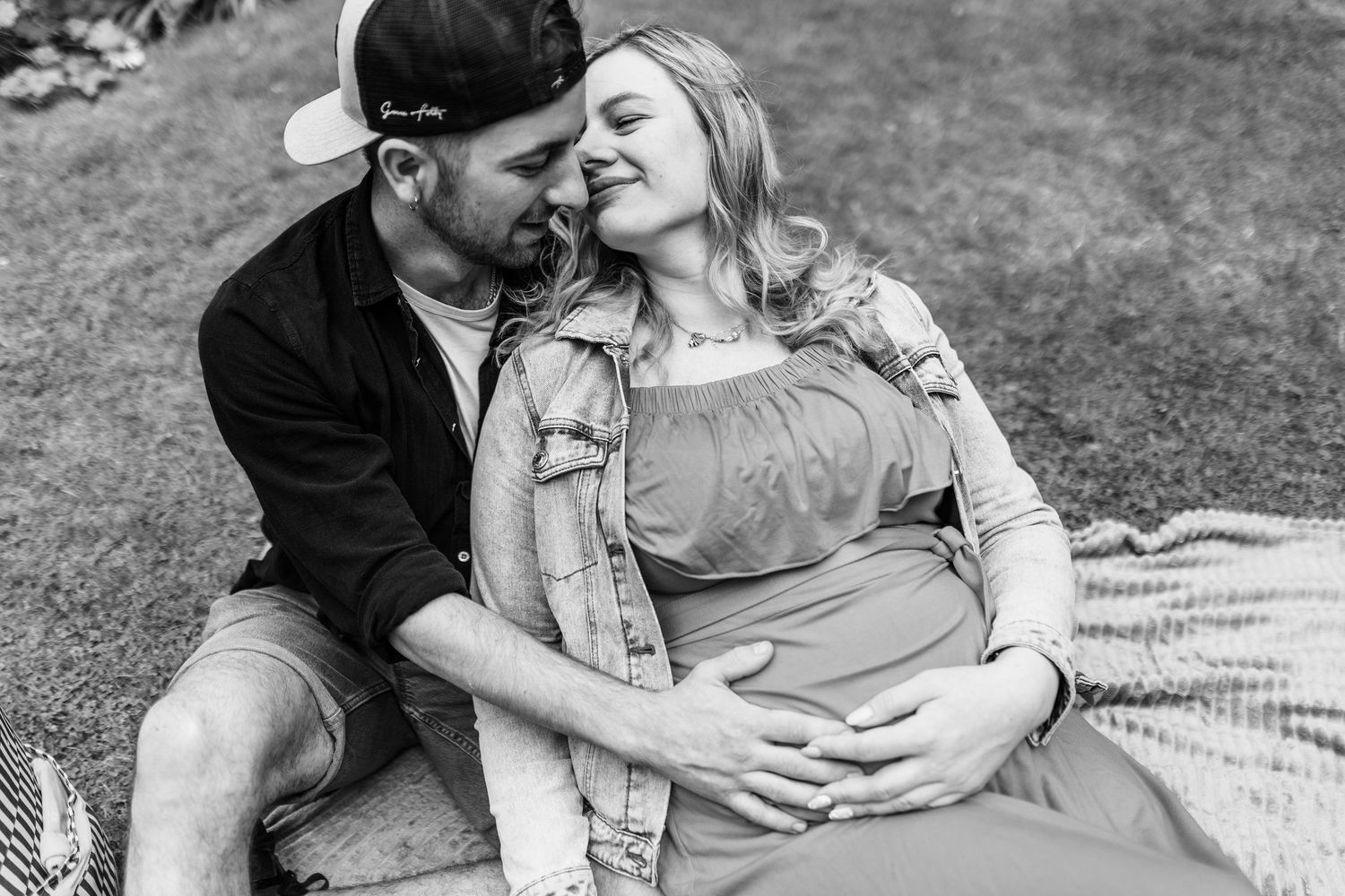 Intimate black and white photo of couple lying on blanket in grass.