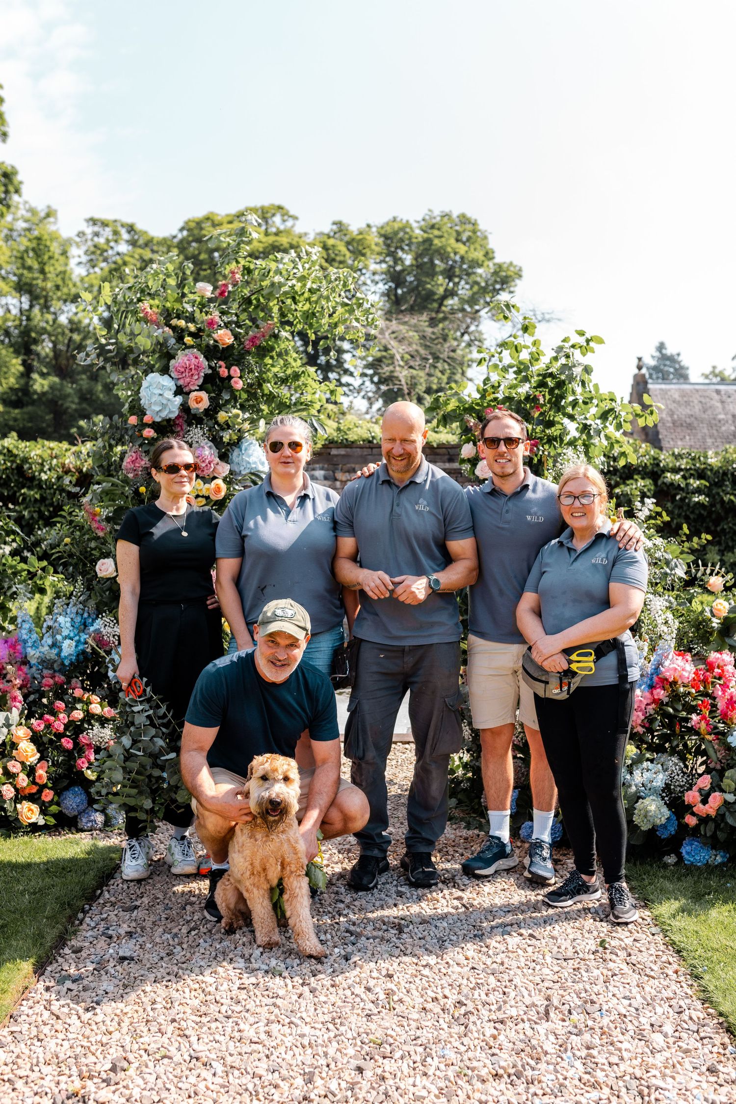 Group photo in front of a blooming flower garden with a dog.