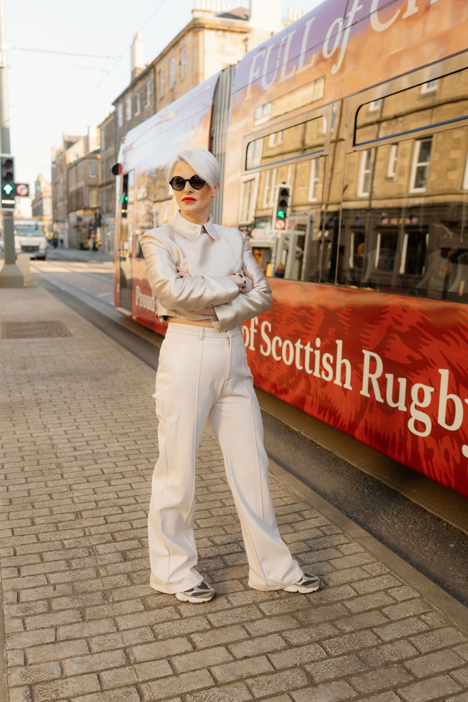 A person in a white outfit strikes dance poses on a cobblestone street in front of a Scottish Rugby sign.