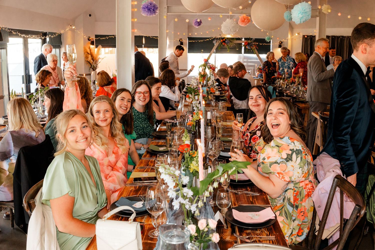 Panoramic view of wedding reception with guests celebrating at decorated tables.