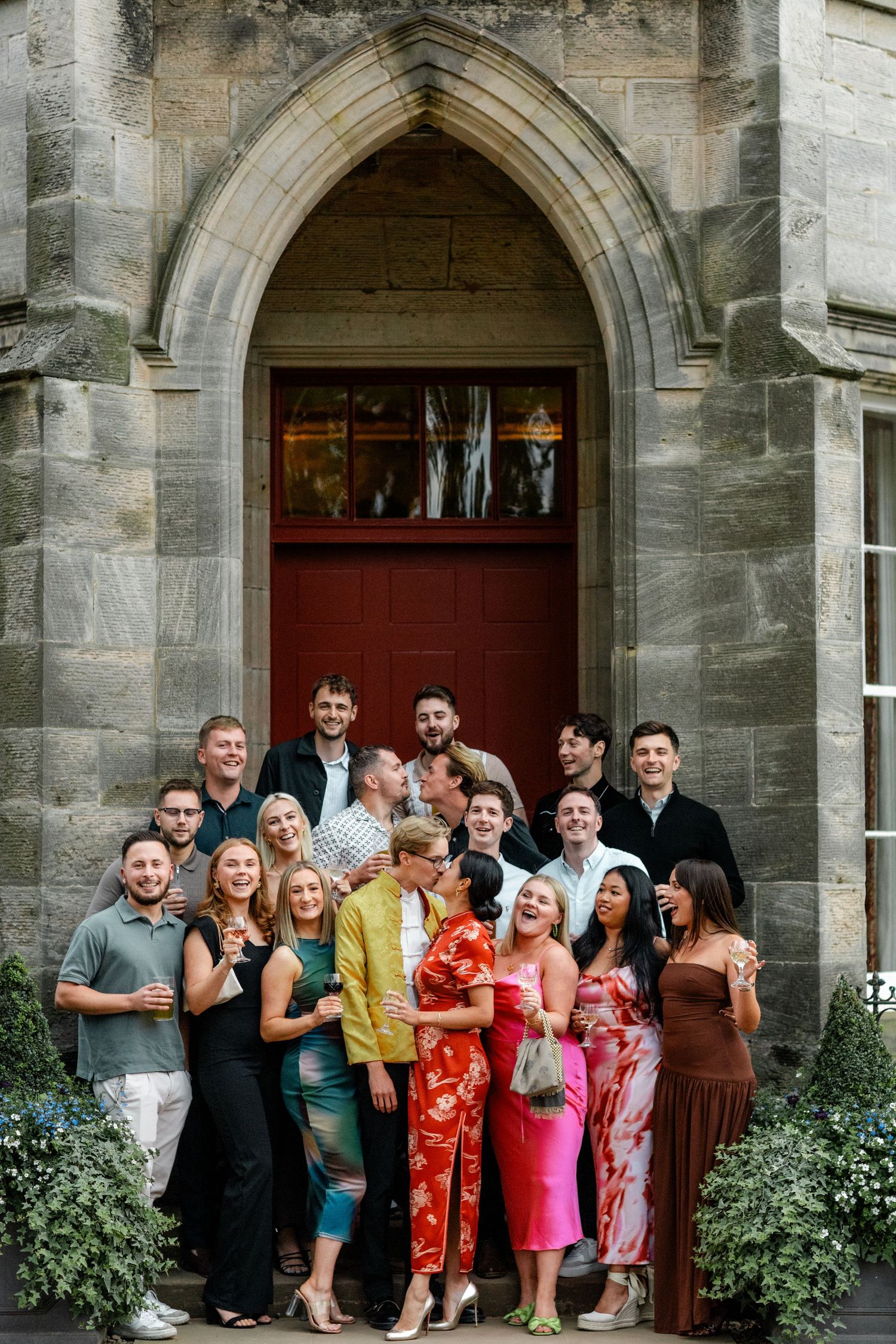 Celebration group shot of wedding guests gathered outside an elegant stone archway entrance.