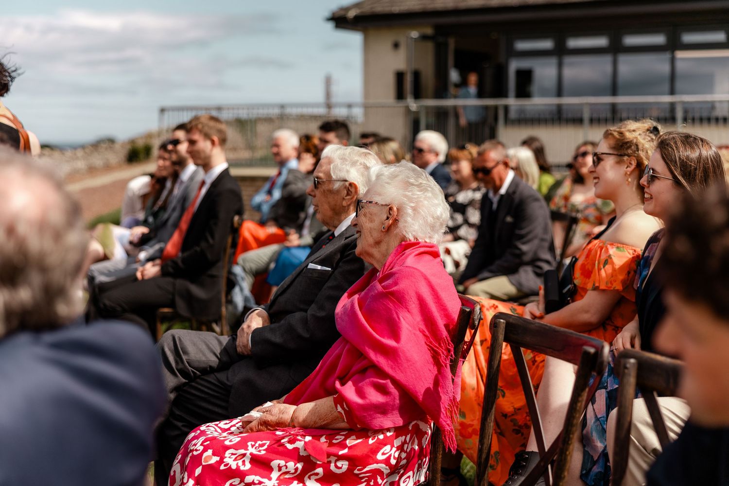 Wedding guests seated in rows at an outdoor ceremony with dramatic cloudy skies.
