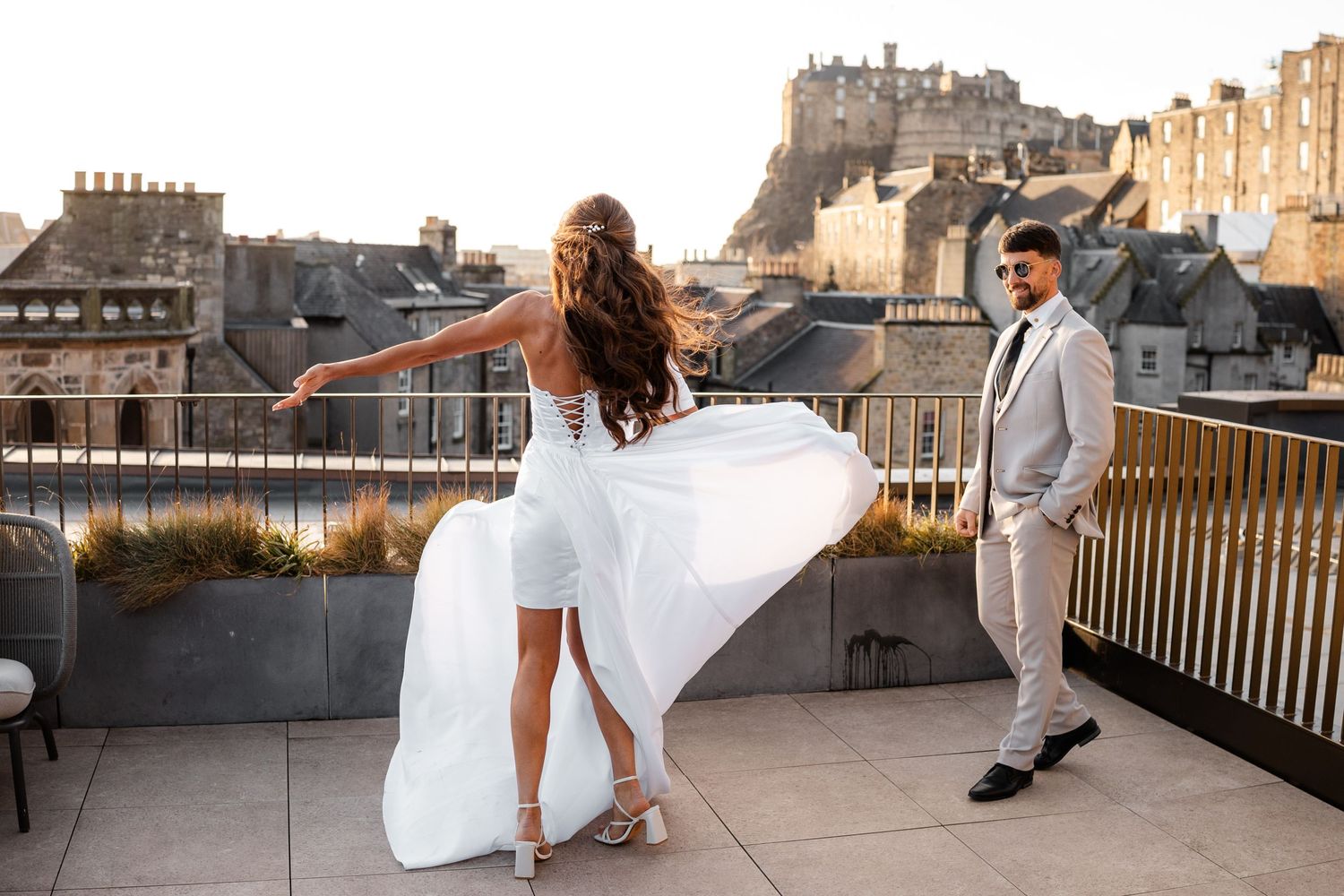 Couple dances and poses on a rooftop terrace with historic buildings in the background.