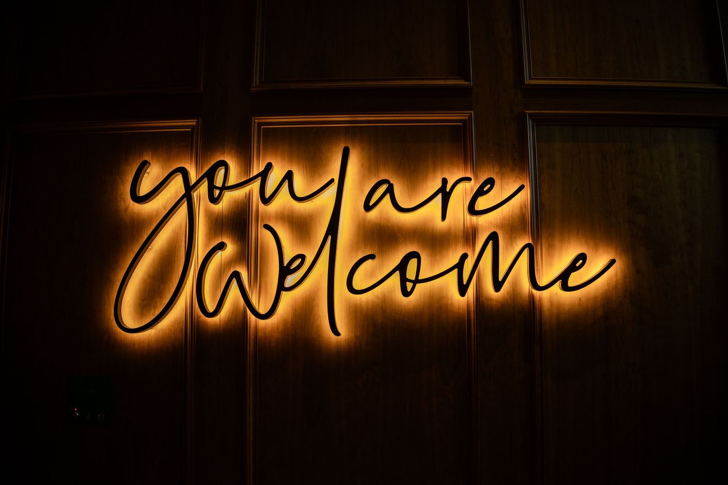 Series of glowing neon welcome signs in warm orange tones against dark background.