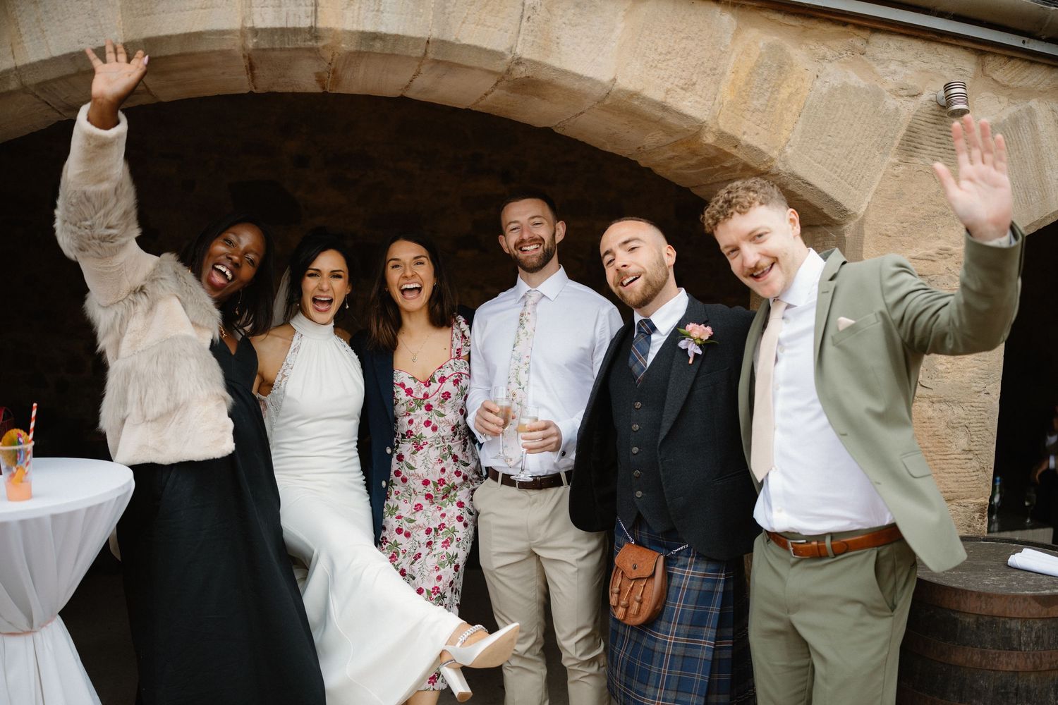 Wedding party poses against stone wall in casual celebratory moment.