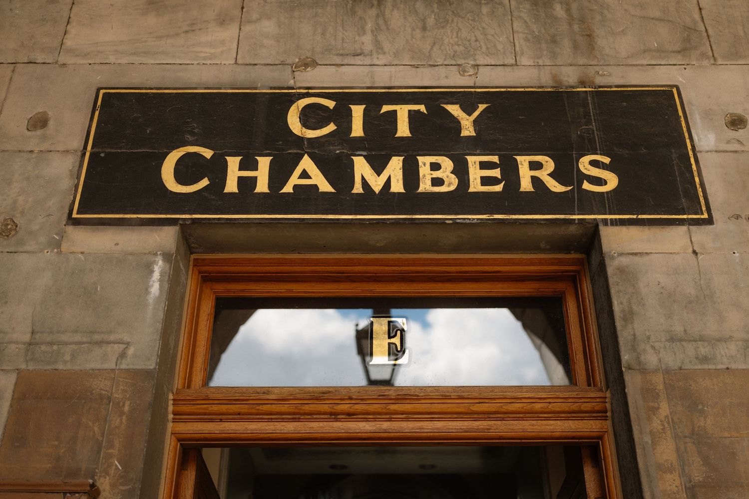 Gold lettered City Chambers sign above a wooden doorway on a stone building facade.
