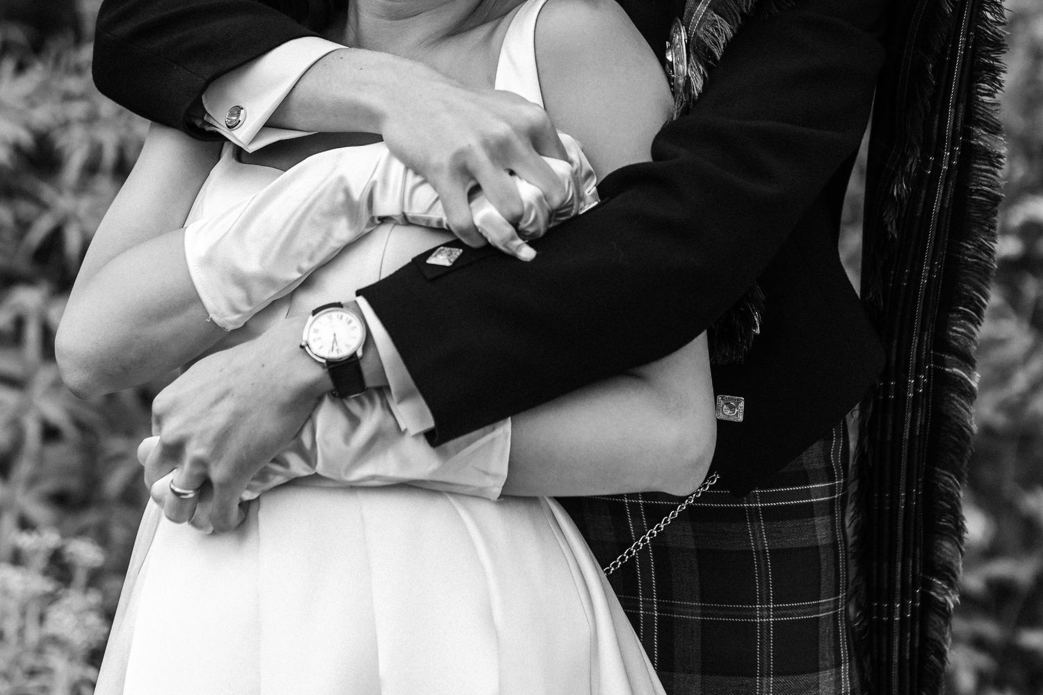 A tender black and white moment showing clasped hands with traditional Scottish and bridal attire.