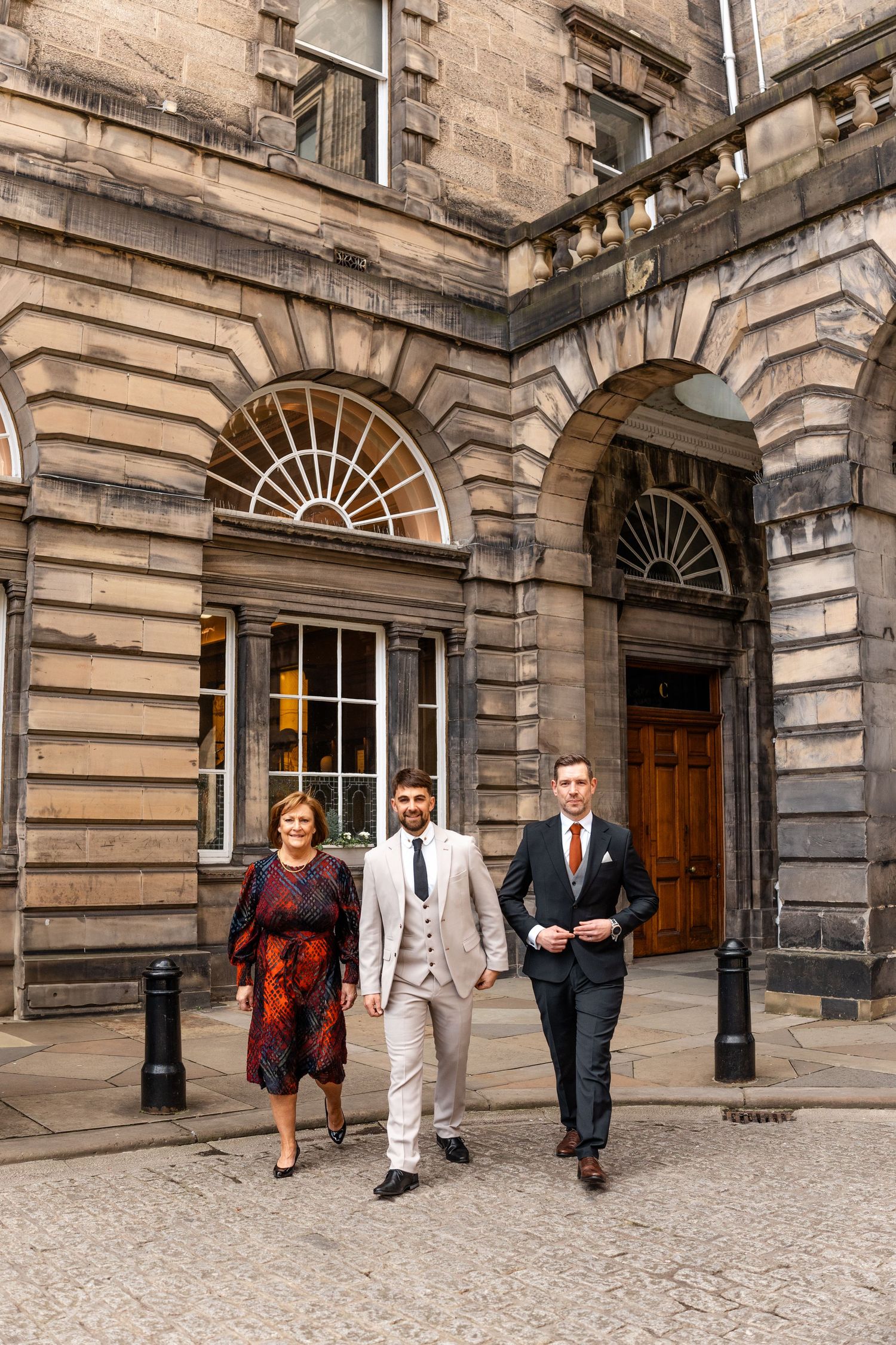 A group walking along the exterior of a grand historic stone building with arched windows.