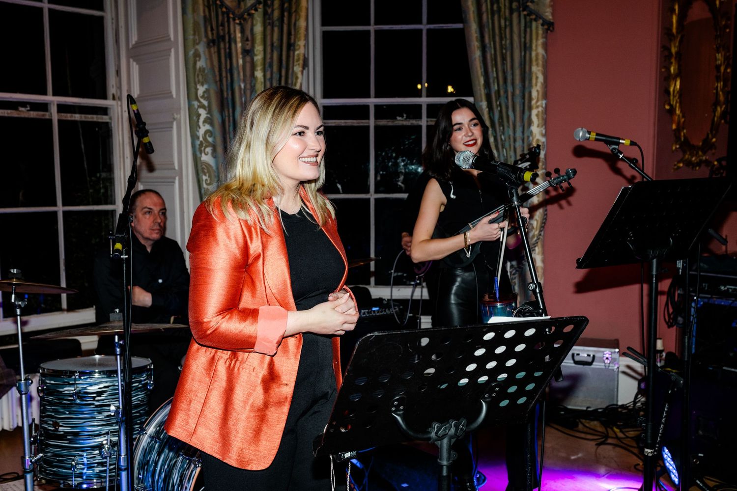Live band performing on stage with instruments and microphones at an evening event.