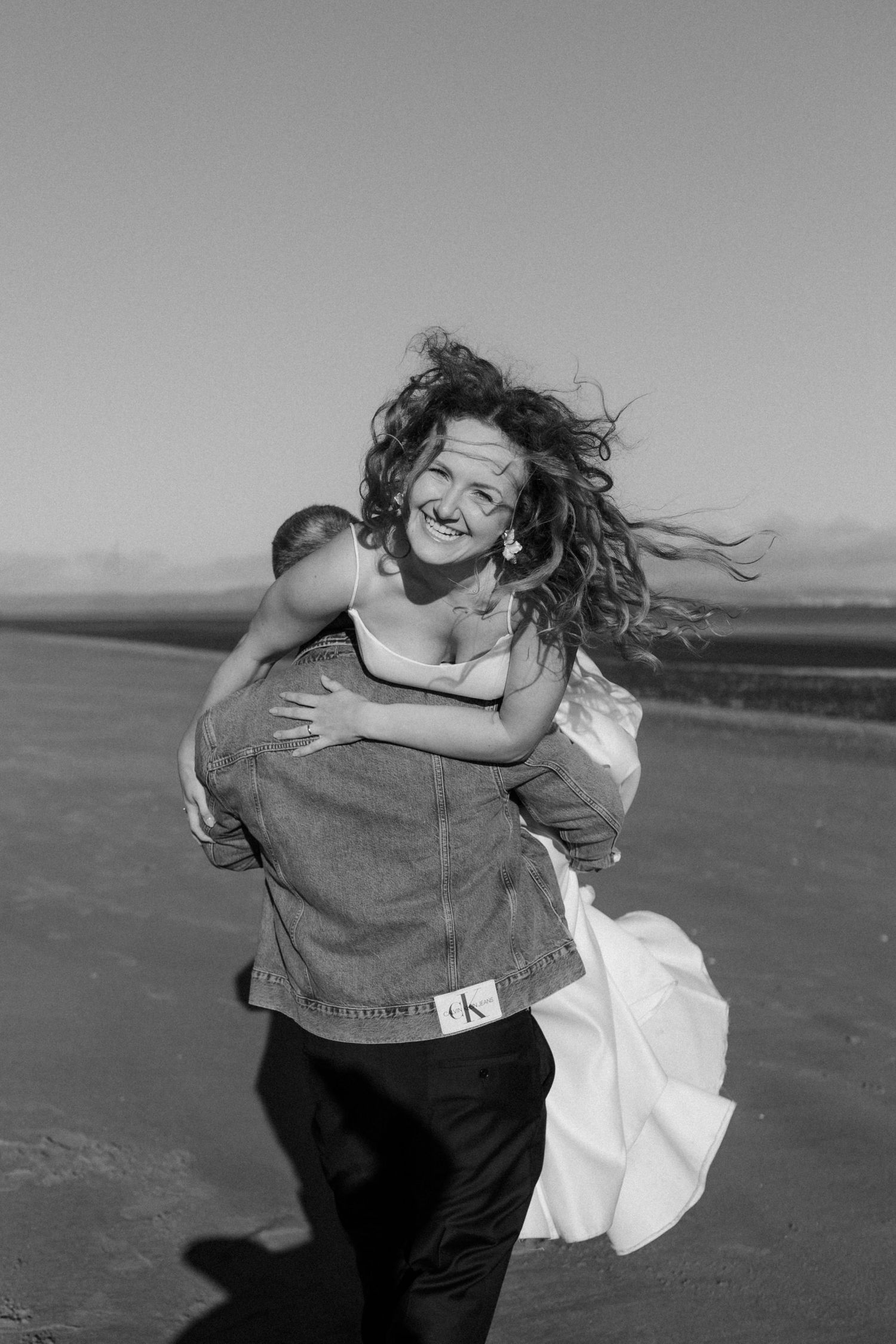 A playful black and white moment captured on a beach with windswept hair.