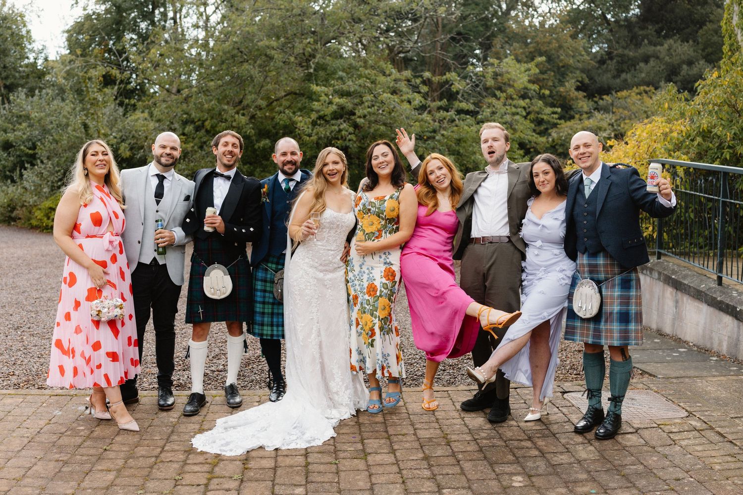 Wedding party group photo outdoors with guests in kilts and colorful dresses celebrating Scottish wedding day.