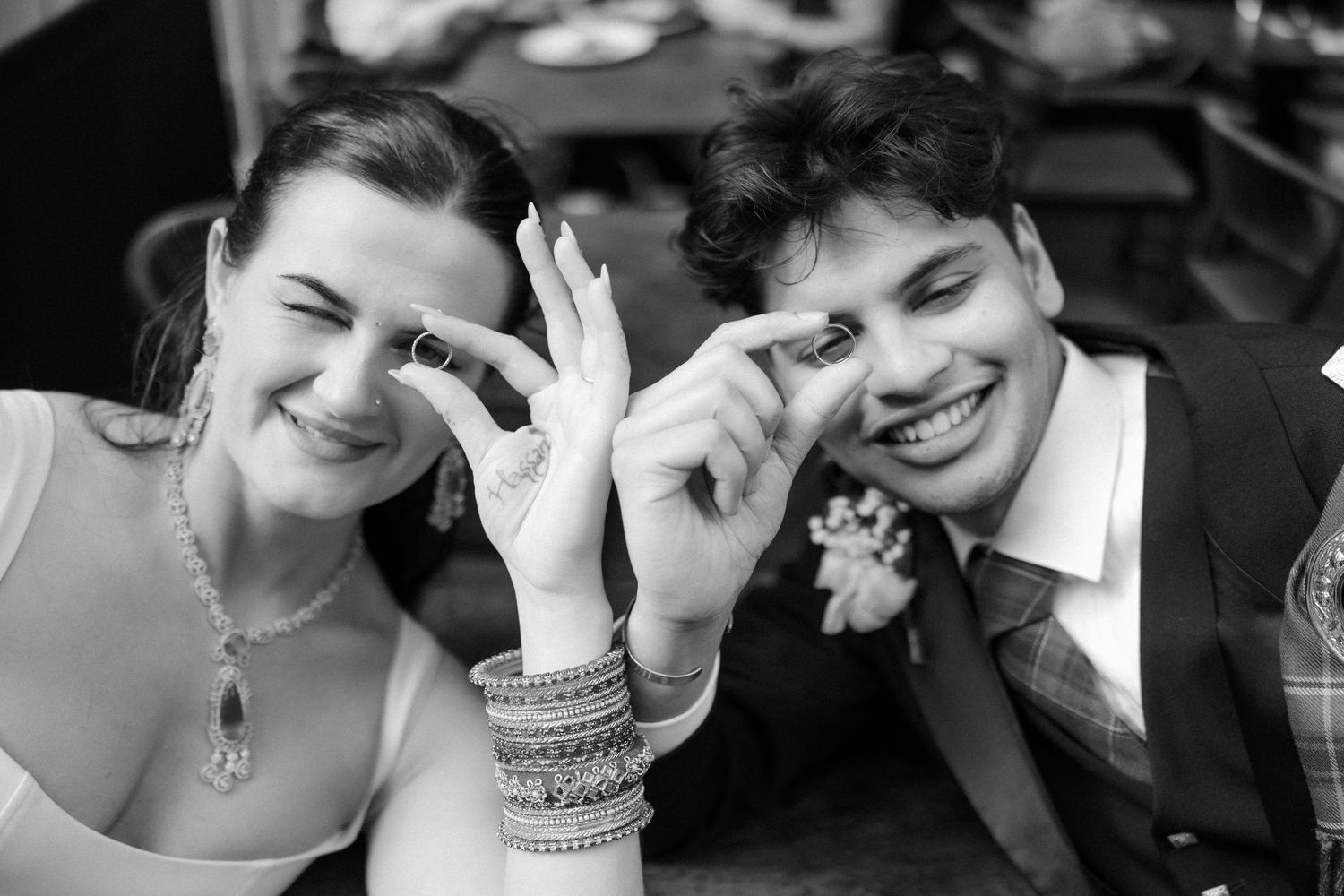 Black and white photo of smiling bride and groom making heart shapes with their fingers.